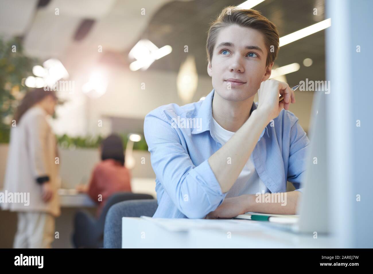 Portrait eines lächelnden jungen Mannes, der trostlos wegschaut, während er mit einem Laptop im Büro arbeitet, Platz für Kopien Stockfoto