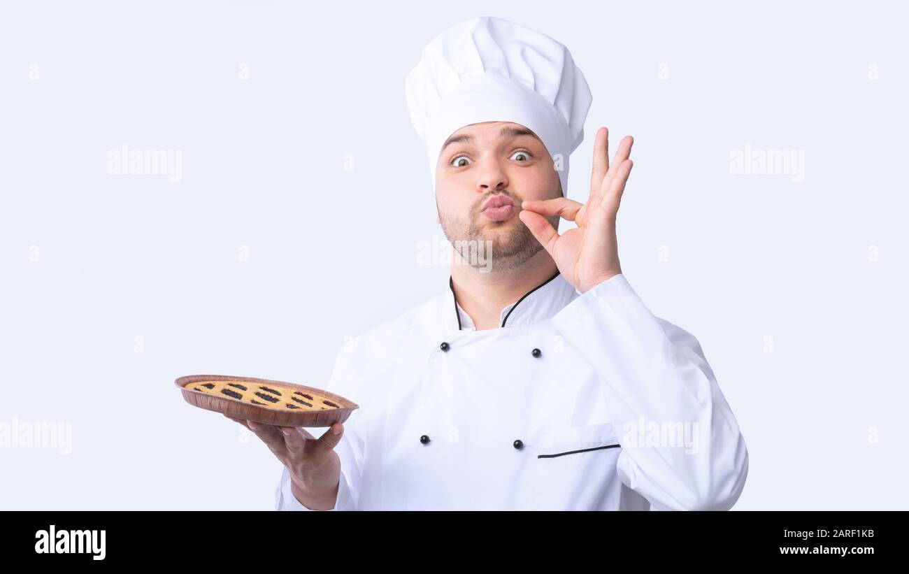 Chefkoch Guy Holding Pie Doing Zip Your Lip Gesture, Studio Stockfoto