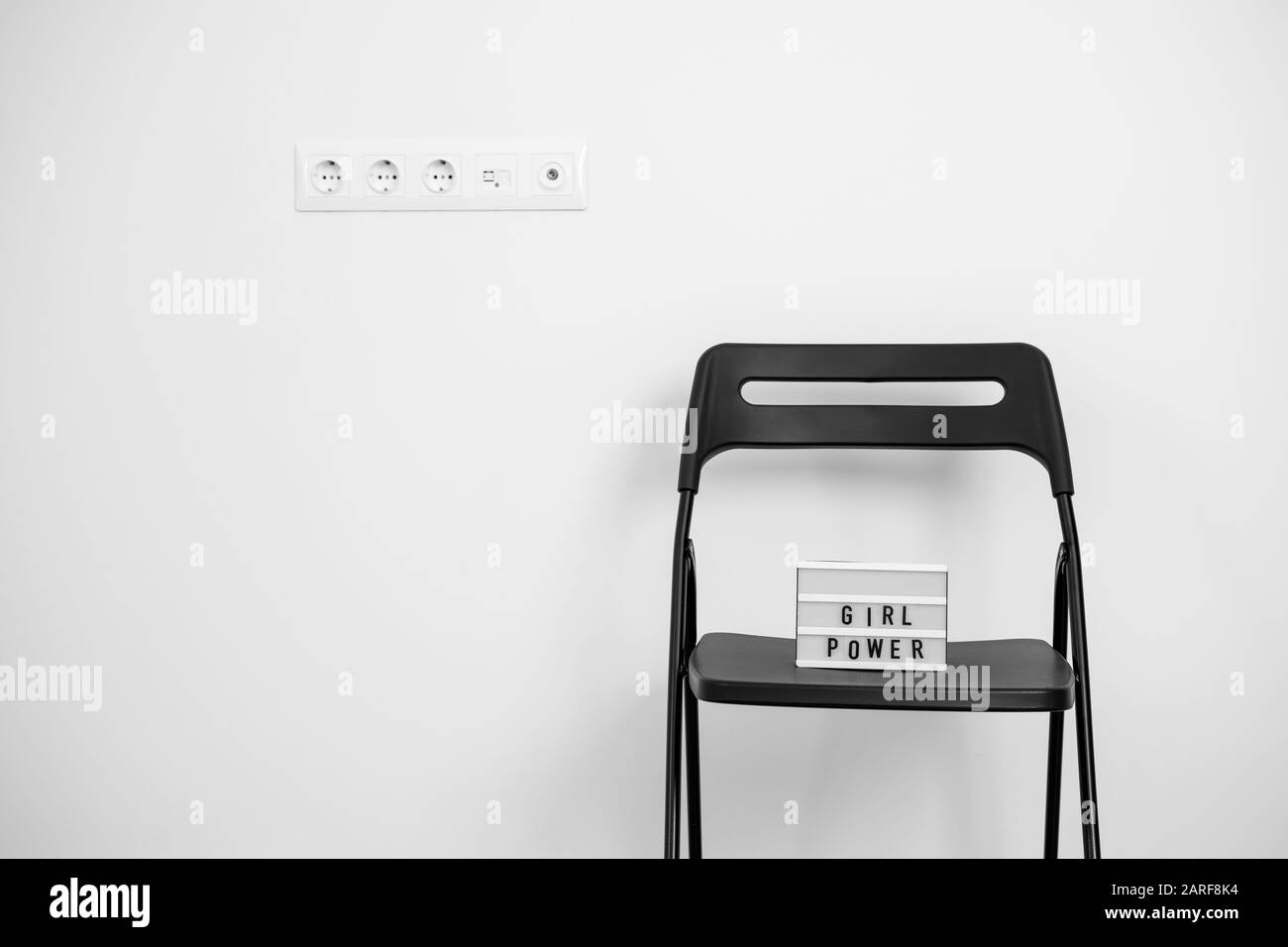 Mädchen Power Text auf dem Leuchtkasten. Weiße Wand und Steckdosen. Blsck Stuhl Stockfoto