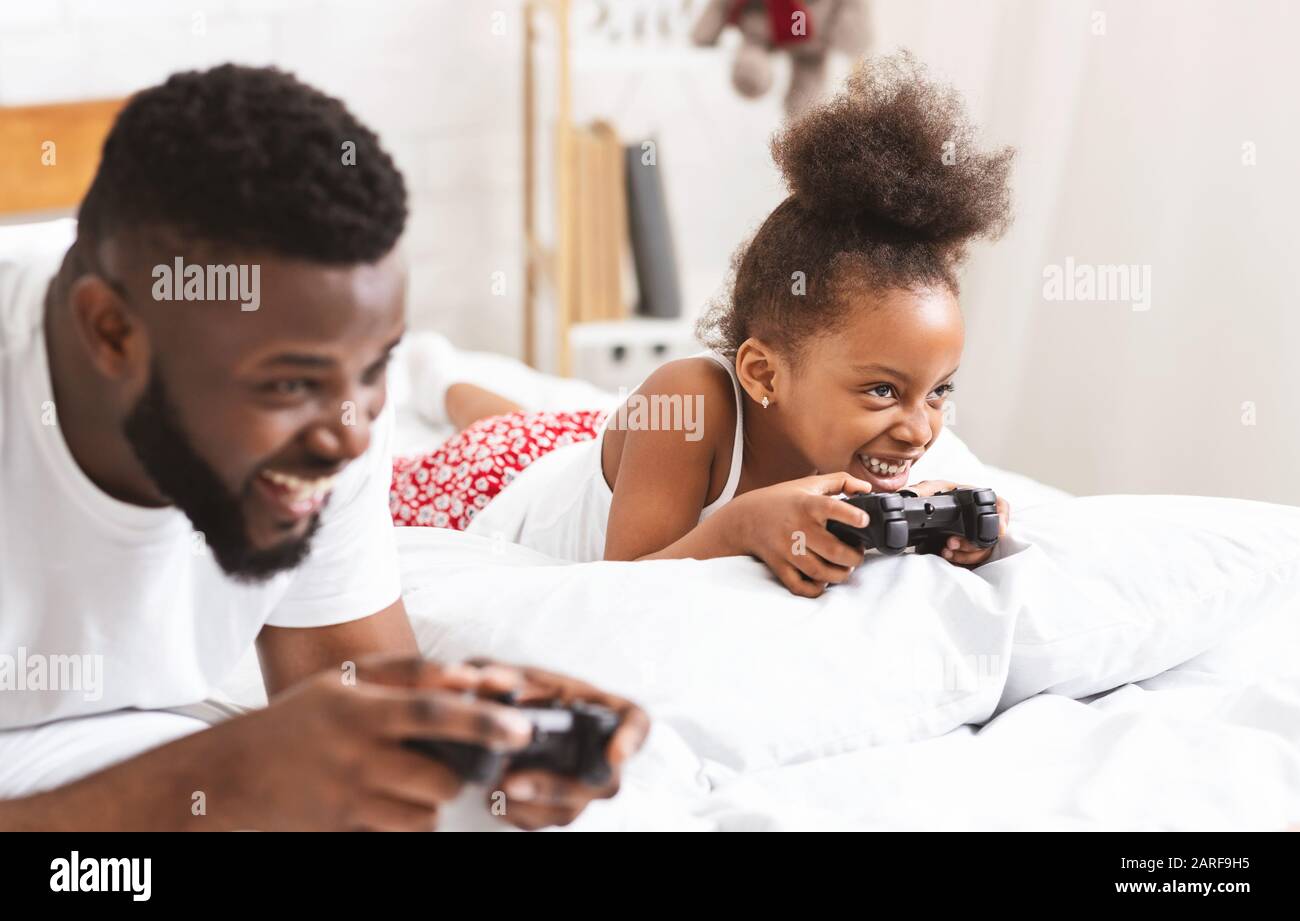 Glücklicher schwarzer Familienvater und Tochter, die Videospiele im Schlafzimmer spielen Stockfoto
