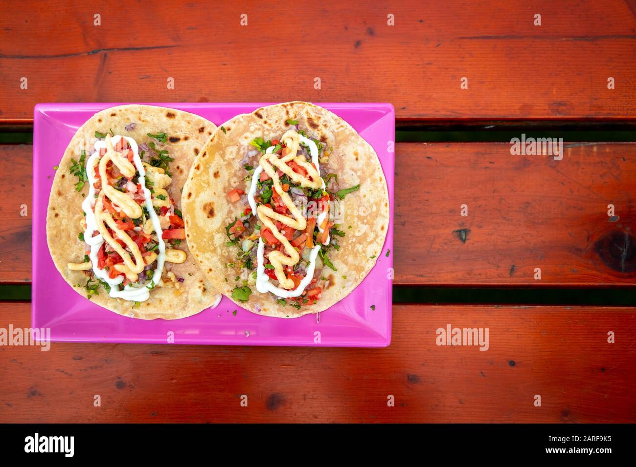 Draufsicht von Tacos. Handgemachte mexikanische Speisen werden in einem rosafarbenen Teller serviert, der auf einer Holzoberfläche platziert ist. Authentisches Würziges Essen. Stockfoto