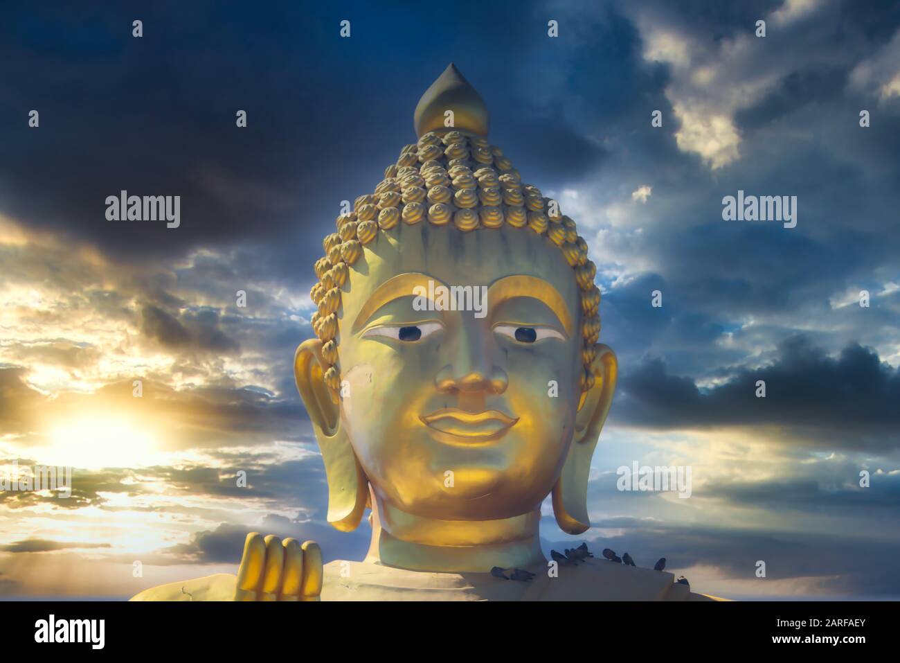 Dieses einzigartige Foto zeigt den goldenen Kopf einer großen Buddha-Statue und einen verträumten Sonnenuntergang mit roten Wolken am Himmel von Hua hin in Thailand. Stockfoto