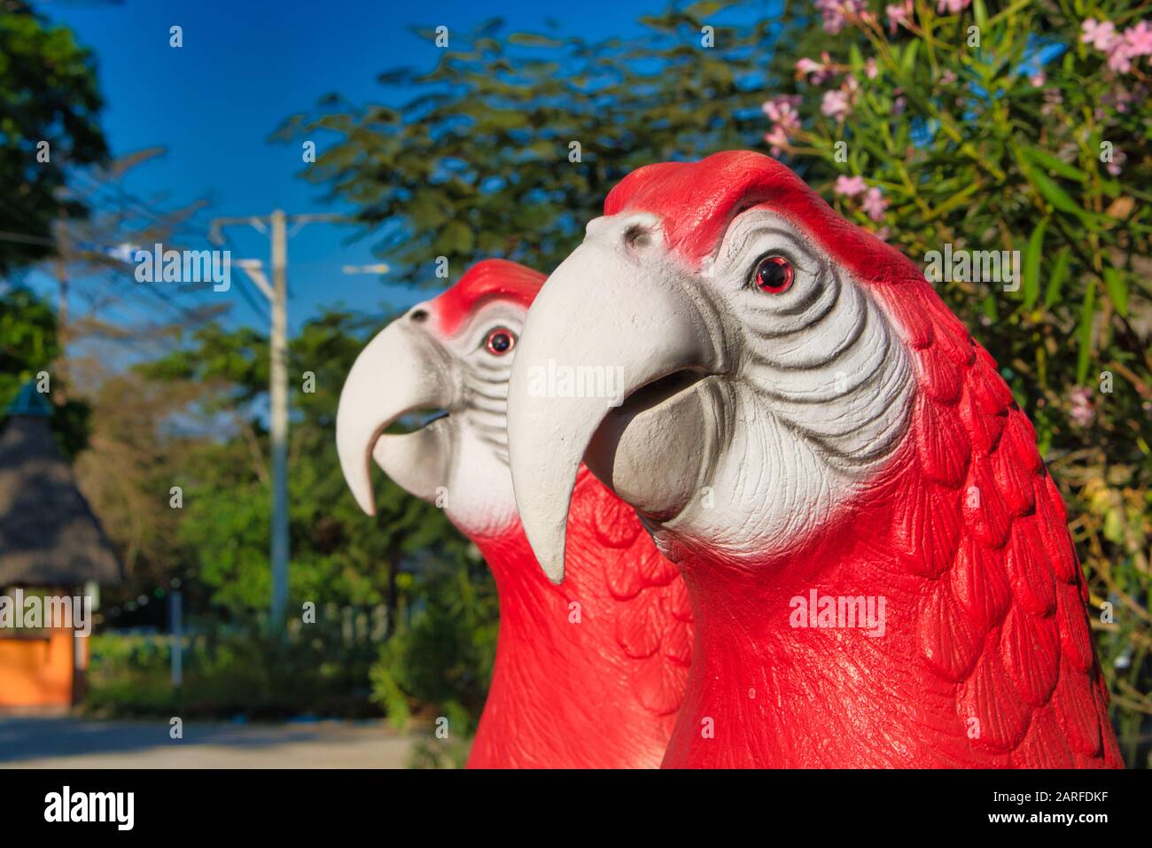 Dieses einzigartige Foto zeigt zwei dekorative Papageienköpfe in rot und weiß, die in einem Garten stehen. Man kann die Details sehr gut sehen. Stockfoto