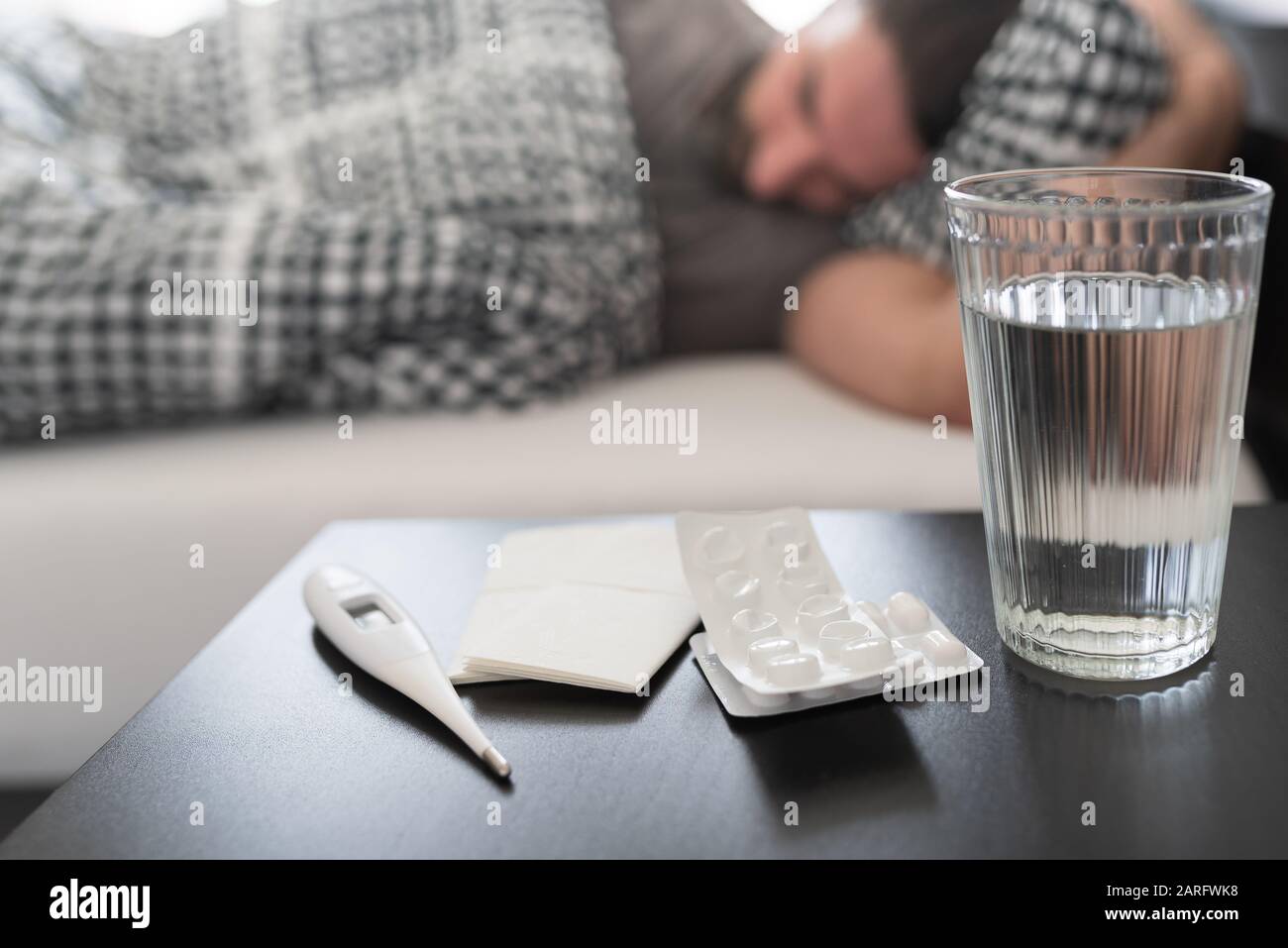 Med, medizinisches Thermometer und Glas Wasser auf Nachttisch gegen kranke Menschen, die an Grippe leiden oder im Bett schlafen Stockfoto