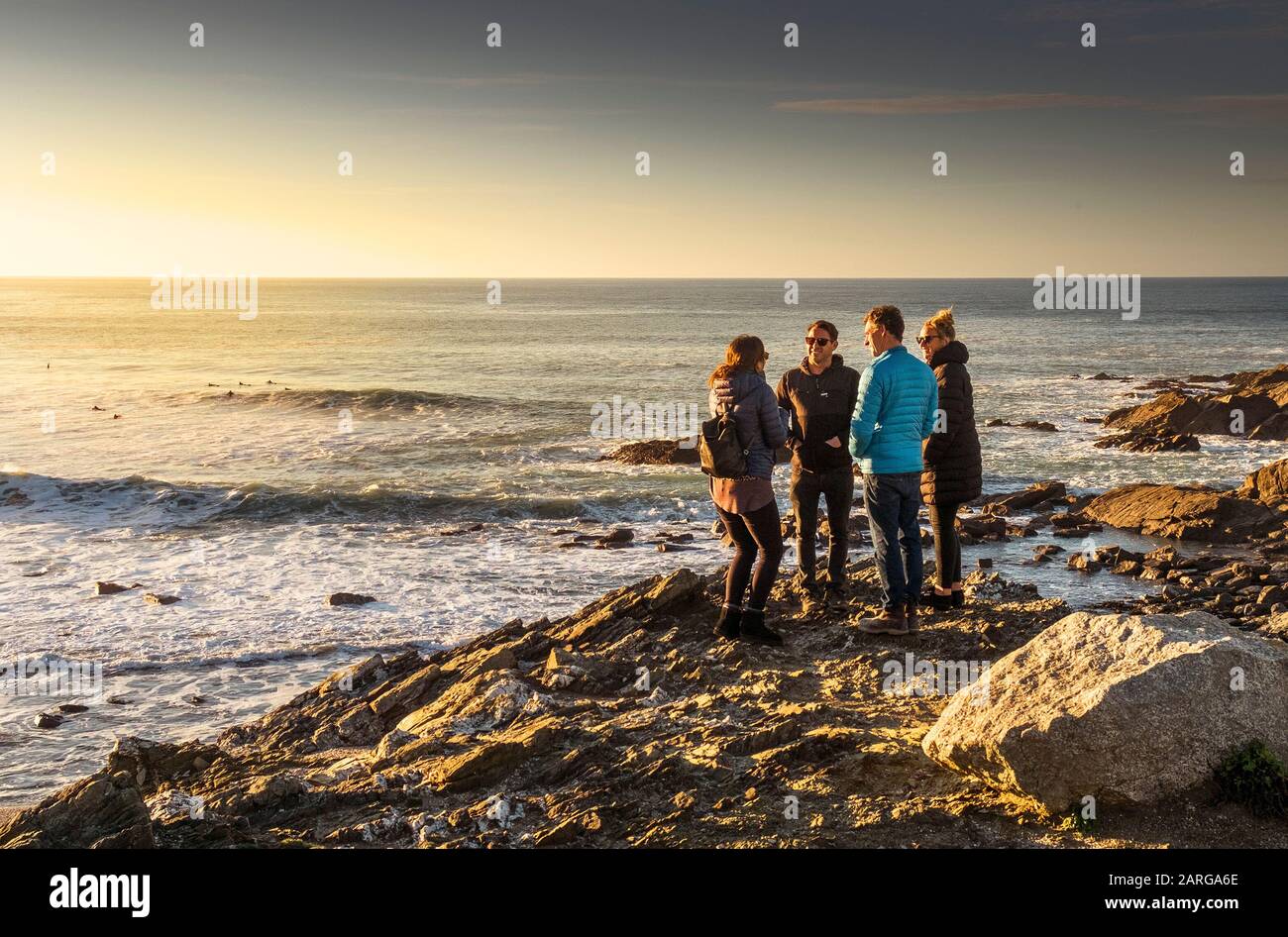 Eine Gruppe von Freunden, die sich unterhalten und auf Felsen mit Blick auf Little Fistral in Newquay in Cornwall stehen. Stockfoto