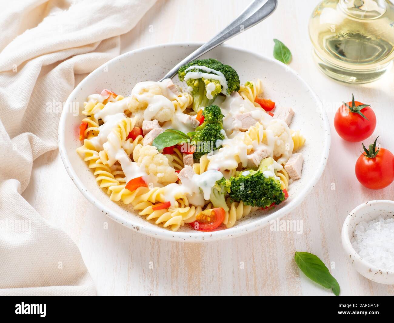 Nudelfusilli mit Gemüse, gekochtem gedämmtem Fleisch, weißer Soße auf weißem Holztisch, kalorienarme Speisen, fettarme Ernährung, Seitenansicht Stockfoto