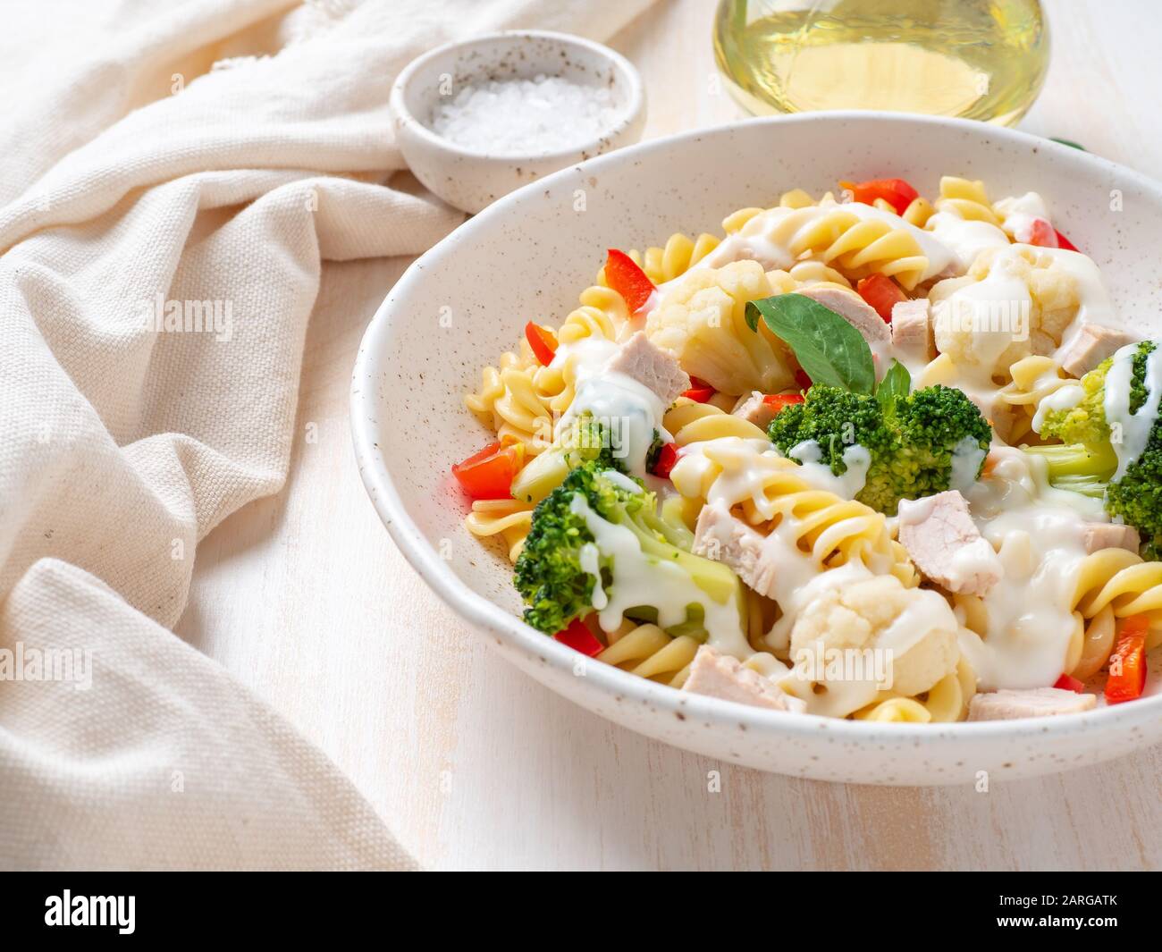 Nudelfusilli mit Gemüse, gekochtem gedämmtem Fleisch, weißer Soße auf weißem Holztisch, kalorienarme Speisen, fettarme Ernährung, Seitenansicht Stockfoto