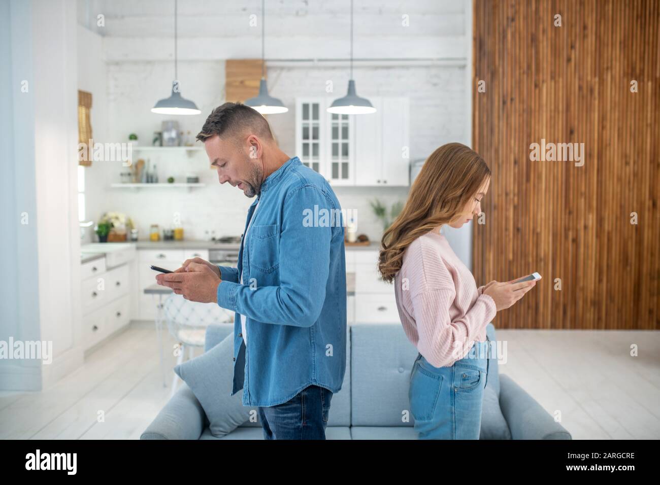 Vater und Tochter lehnen sich zurück, um auf ihre Smartphones zu schauen. Stockfoto