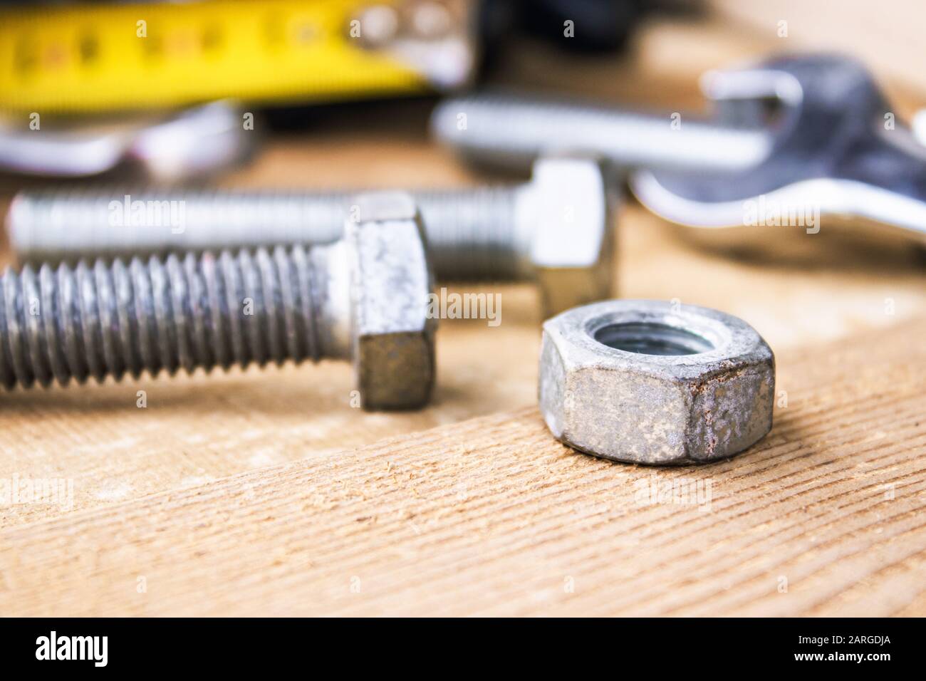 Ein verstellbarer Schraubenschlüssel liegt in der Nähe der Schrauben und Muttern der Unterlegscheibe vor dem Hintergrund von Holzplatten. Das Konzept der Werkzeuge und Reparaturarbeiten. Stockfoto