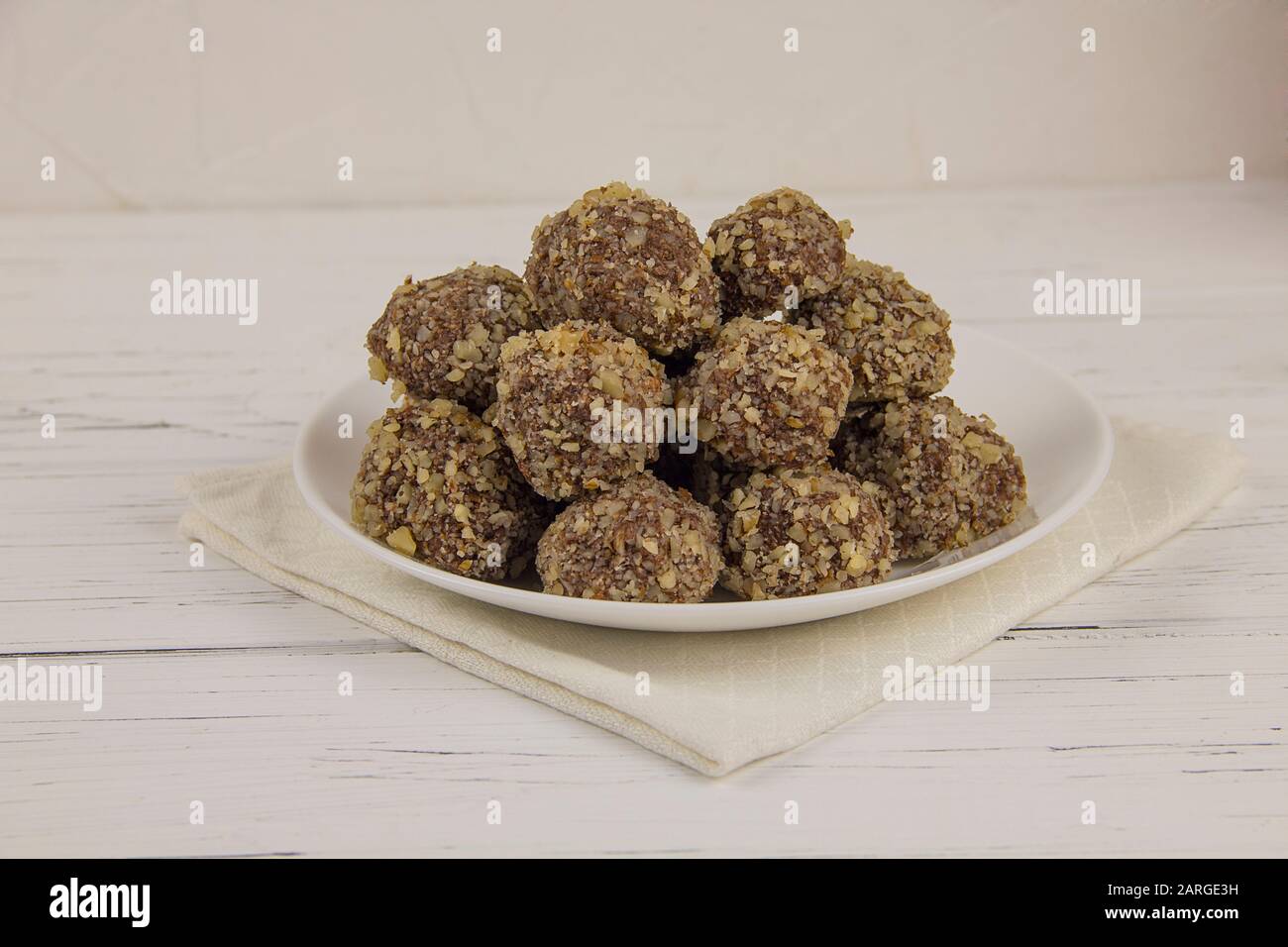 Energiekugeln hausgemachte gesunde Süßigkeiten ohne Zucker in einem weißen Teller auf einer BaumwollServiette auf weißem Holzhintergrund Stockfoto