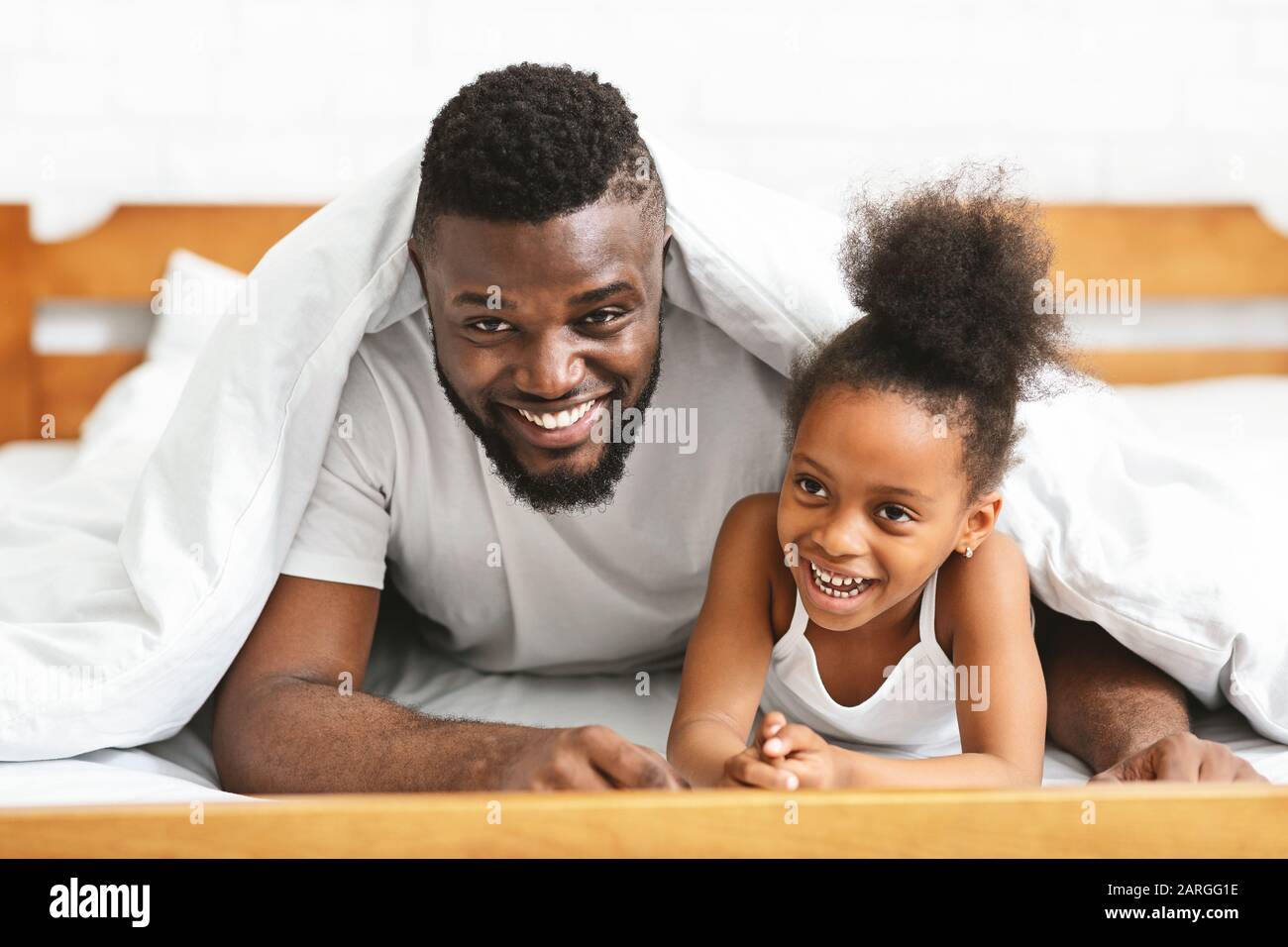 Lächelnder schwarzer Familienvater und Tochter unter Decke legen Stockfoto