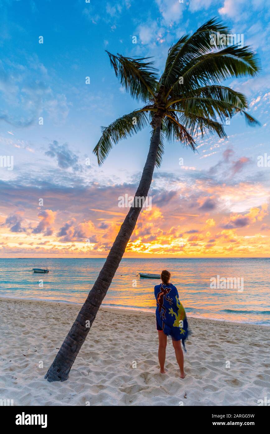 Rückansicht der Frau mit Sarong, die den Ozean bei Sonnenuntergang am Strand mit Palmen bewundert, Le Morne brabant, Black River, Mauritius, Indischer Ozean, Afrika Stockfoto