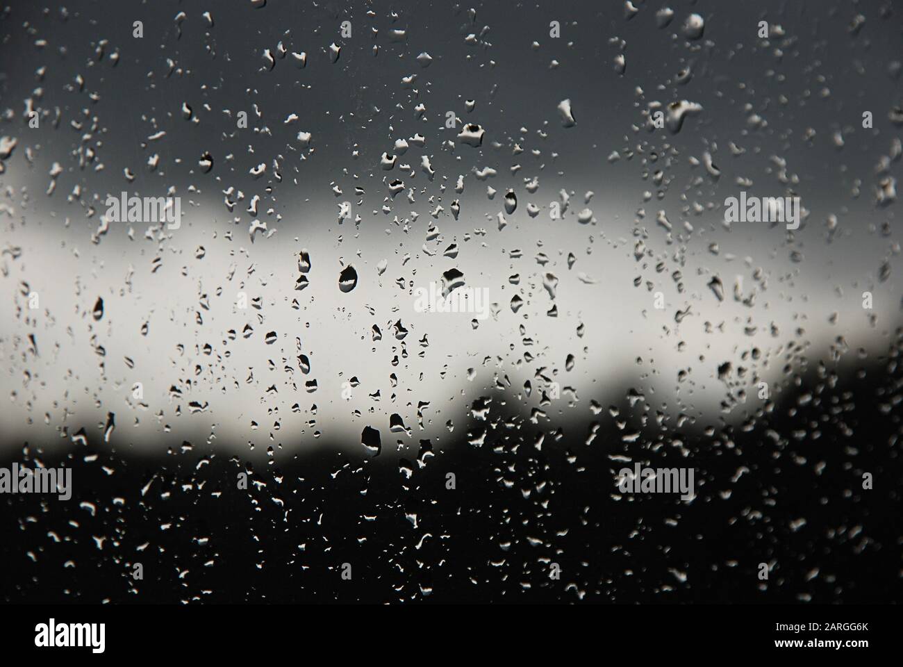 Regentropfen im Fensterbereich. Schwarzer, grauer, weißer Farbverlauf auf unscharfem Hintergrund. Bewölktes Regenwetter außerhalb des Fensters. Kühlung, Regen, schlechtes Wetter Stockfoto