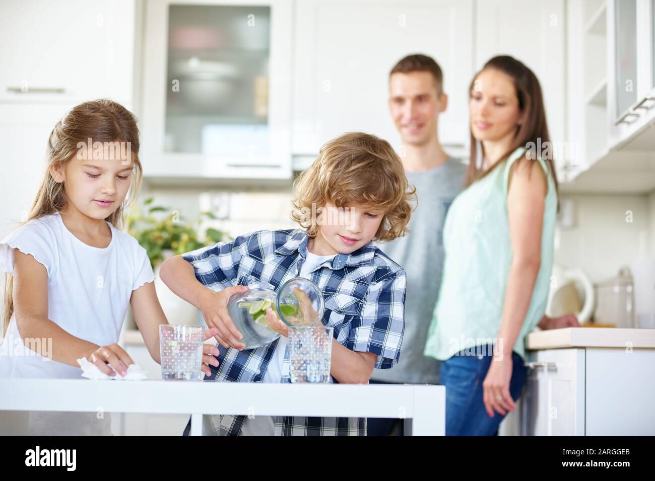 Zwei Kinder trinken in der Küche unter Aufsicht ihrer Eltern Wasser mit frischem Limes Stockfoto