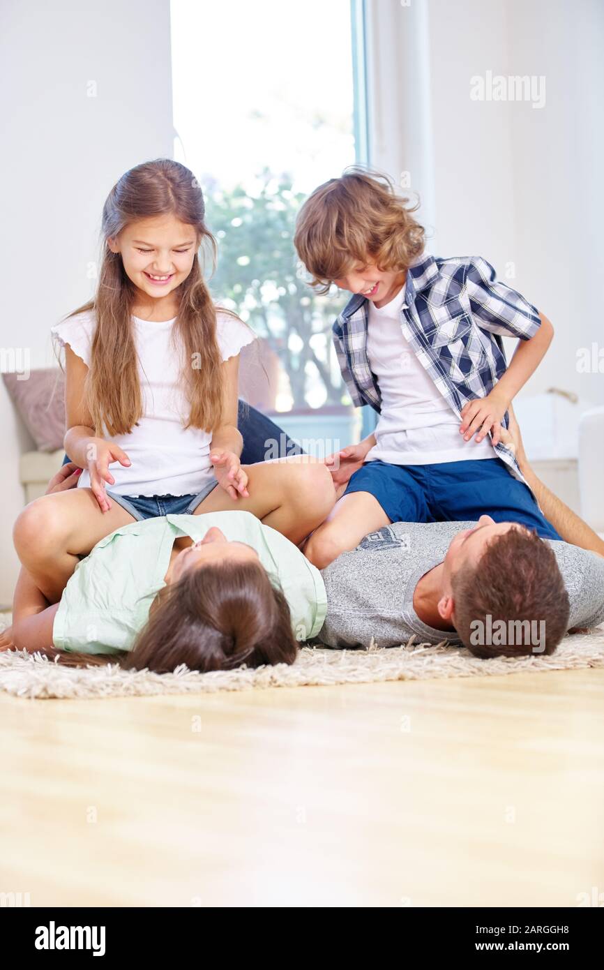 Zwei glückliche Kinder spielen und rompeln mit ihren Eltern im Wohnzimmer Stockfoto