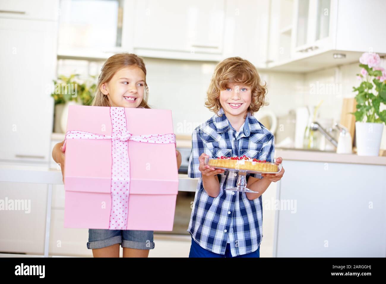 Zwei glückliche Kinder mit Geschenk und Kuchen zum Geburtstag in der Küche Stockfoto