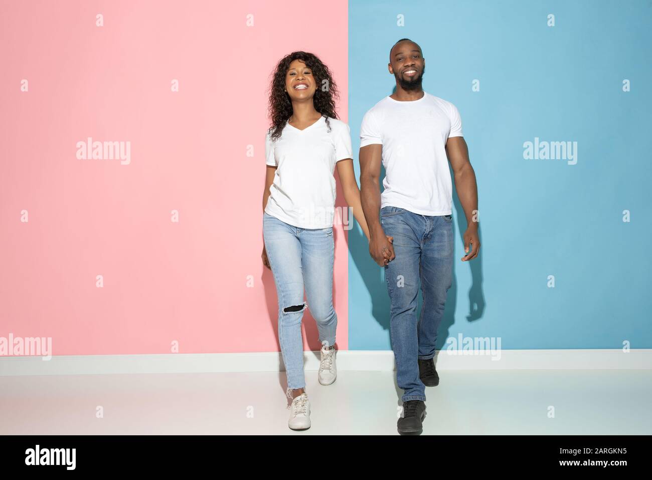 Romantisches gehen. Junger emotionaler Mann und Frau in legerer Kleidung auf pinkfarbenem und blauem bicolored Hintergrund. Konzept der menschlichen Emotionen, Gesichtsausweisung, Beziehungen, Anzeige. Wunderschönes afro-amerikanisches Paar. Stockfoto