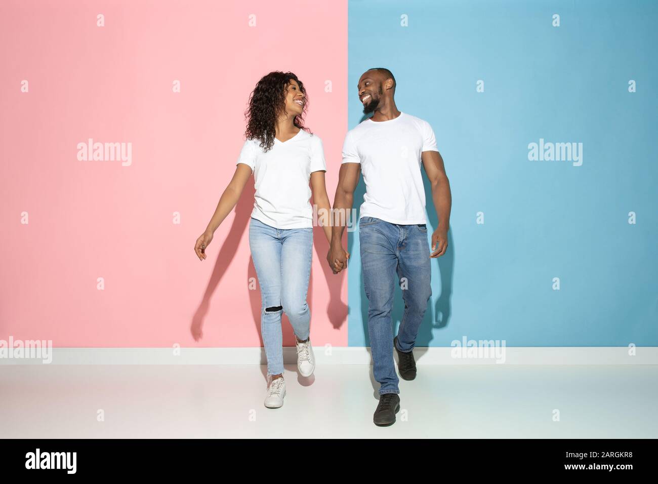 Romantisches gehen. Junger emotionaler Mann und Frau in legerer Kleidung auf pinkfarbenem und blauem bicolored Hintergrund. Konzept der menschlichen Emotionen, Gesichtsausweisung, Beziehungen, Anzeige. Wunderschönes afro-amerikanisches Paar. Stockfoto