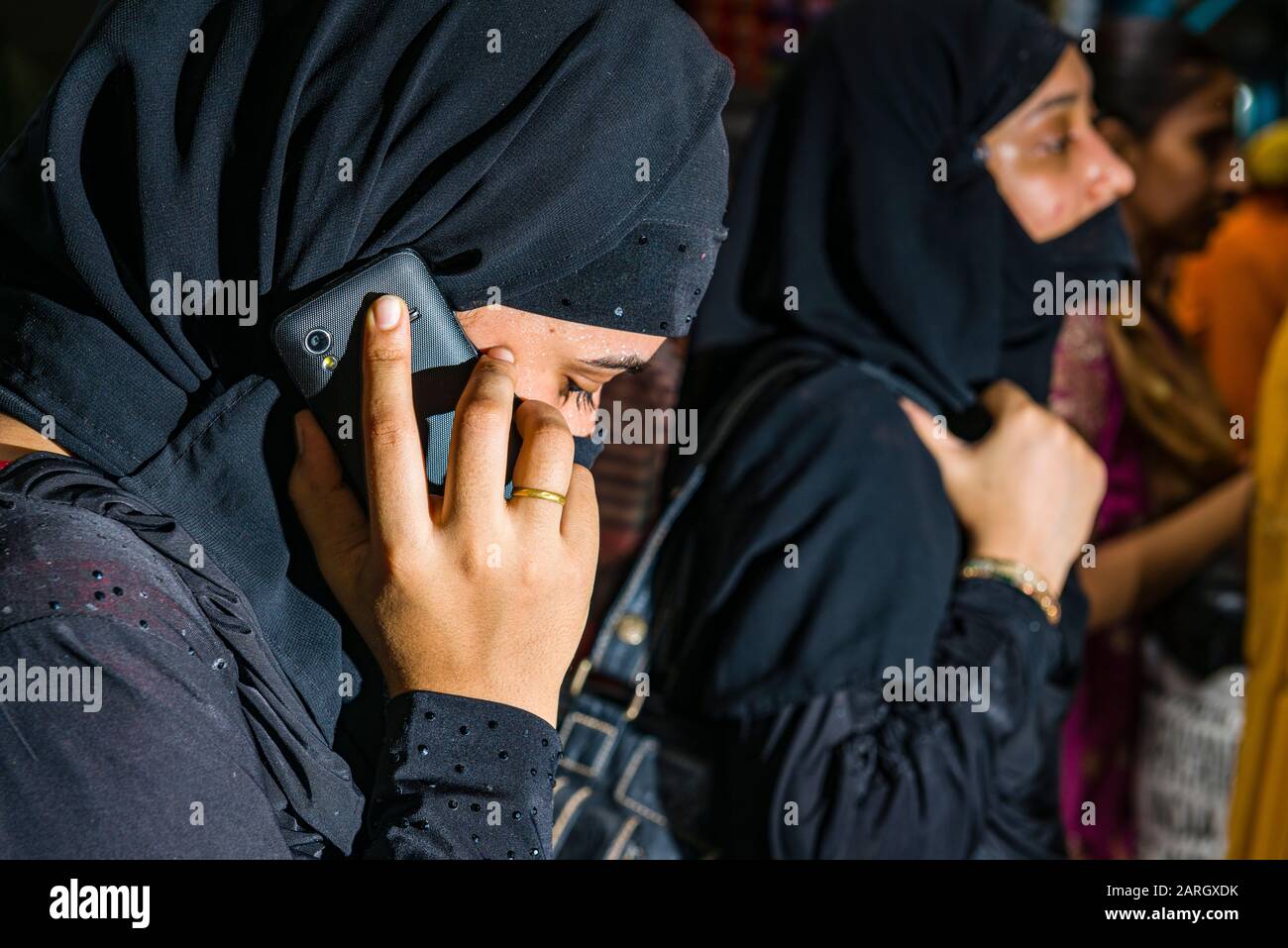 Eine muslimische Frau, die mit Rückenkleidung und Schleier bedeckt ist, benutzt ihr Handy Stockfoto