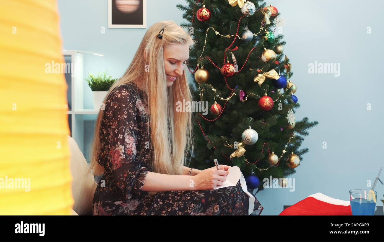 Nahaufnahme Der Lachelnden Jungen Dame Die Einen Brief An Den Weihnachtsmann Schreibt Sie Sitzt Auf Dem Sofa In Der Nahe Des Weihnachtsbaums Und Der Grossen Stehlampe Profilansicht Elemente Dieses Bildes Das Von