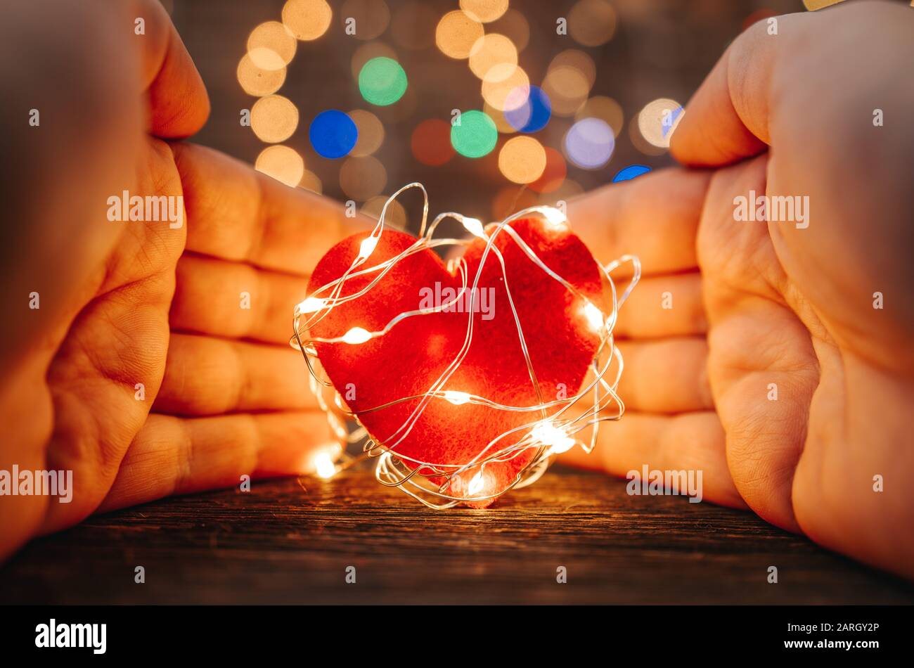 Halten Sie eine rote Herzform, die mit LED-Lampen auf Holz- und Bokeh-Lichtern bedeckt ist. Valentines Tag- und Romanzkonzept Stockfoto