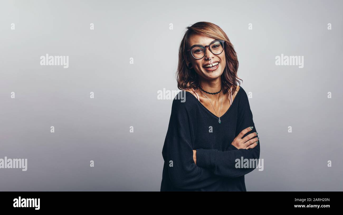 Porträt einer lächelnden Frau, die mit gekreuzten Armen auf die Kamera blickt. Lächelnde Frau in Brillen isoliert auf grauem Hintergrund. Stockfoto