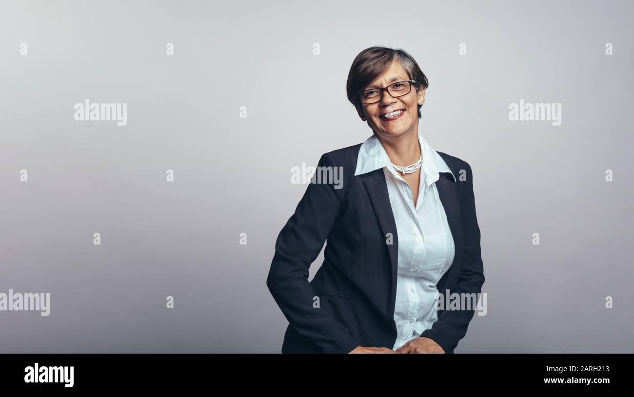 Senior-Geschäftsfrau isoliert auf grauem Hintergrund mit Blick auf die Kamera. Lächelnde Senior-Unternehmerin in formeller Geschäftskleidung. Stockfoto
