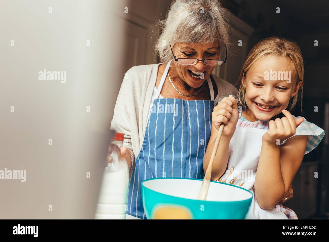 Glückliche Großmutter und Kind, die einen Kuchenteig zu Hause mischten. Fröhliches kleines Mädchen, das den Teig in einer Schüssel rührte, wobei ihre Granny an ihrer Seite stand. Stockfoto