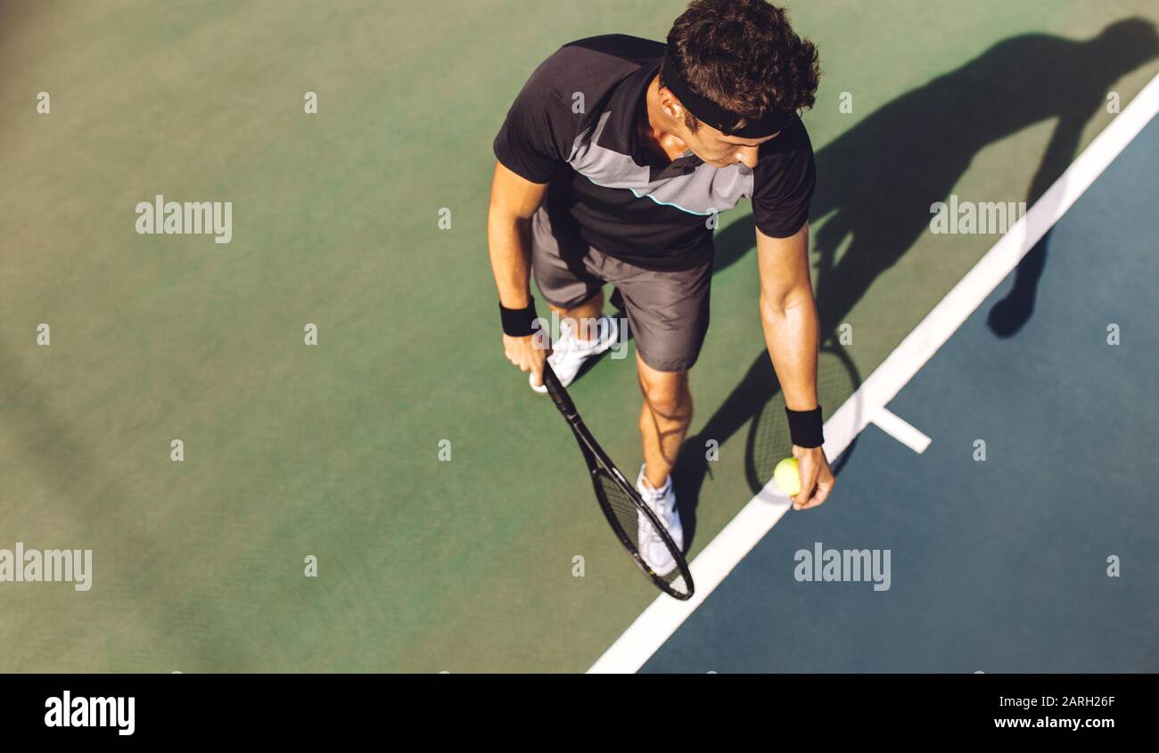 Draufsicht auf einen jungen Tennisspieler mit Schläger, der bereit ist, einen Tennisball zu servieren. Profispieler, der an der Grundlinie steht und den Tennisschläger hält Stockfoto