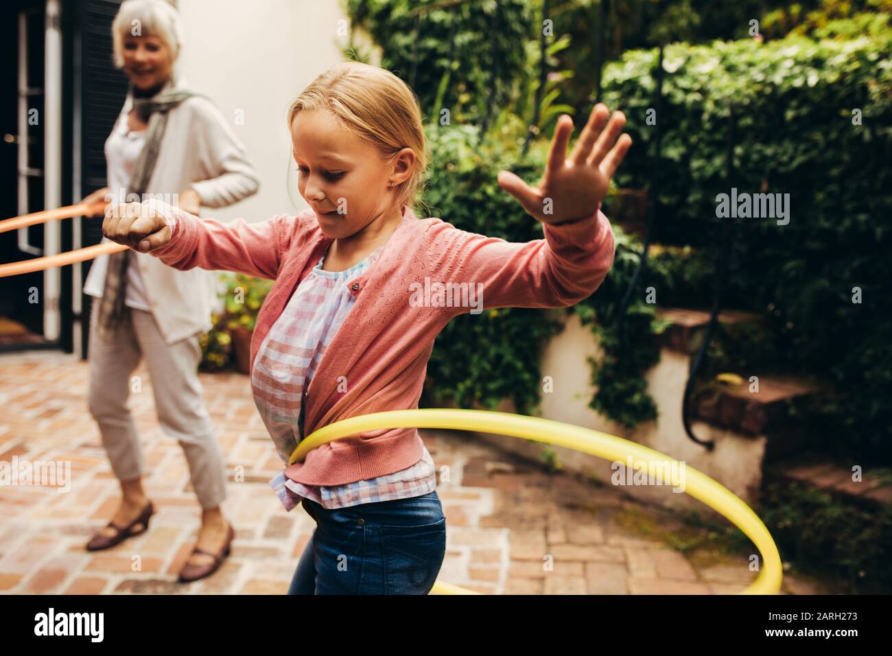 Mädchen, die mit einem Hoopla-Ring in ihrem Hinterhof spielen. Granny und Kind üben, einen Hula-Hoop um ihre Taille zu drehen. Stockfoto