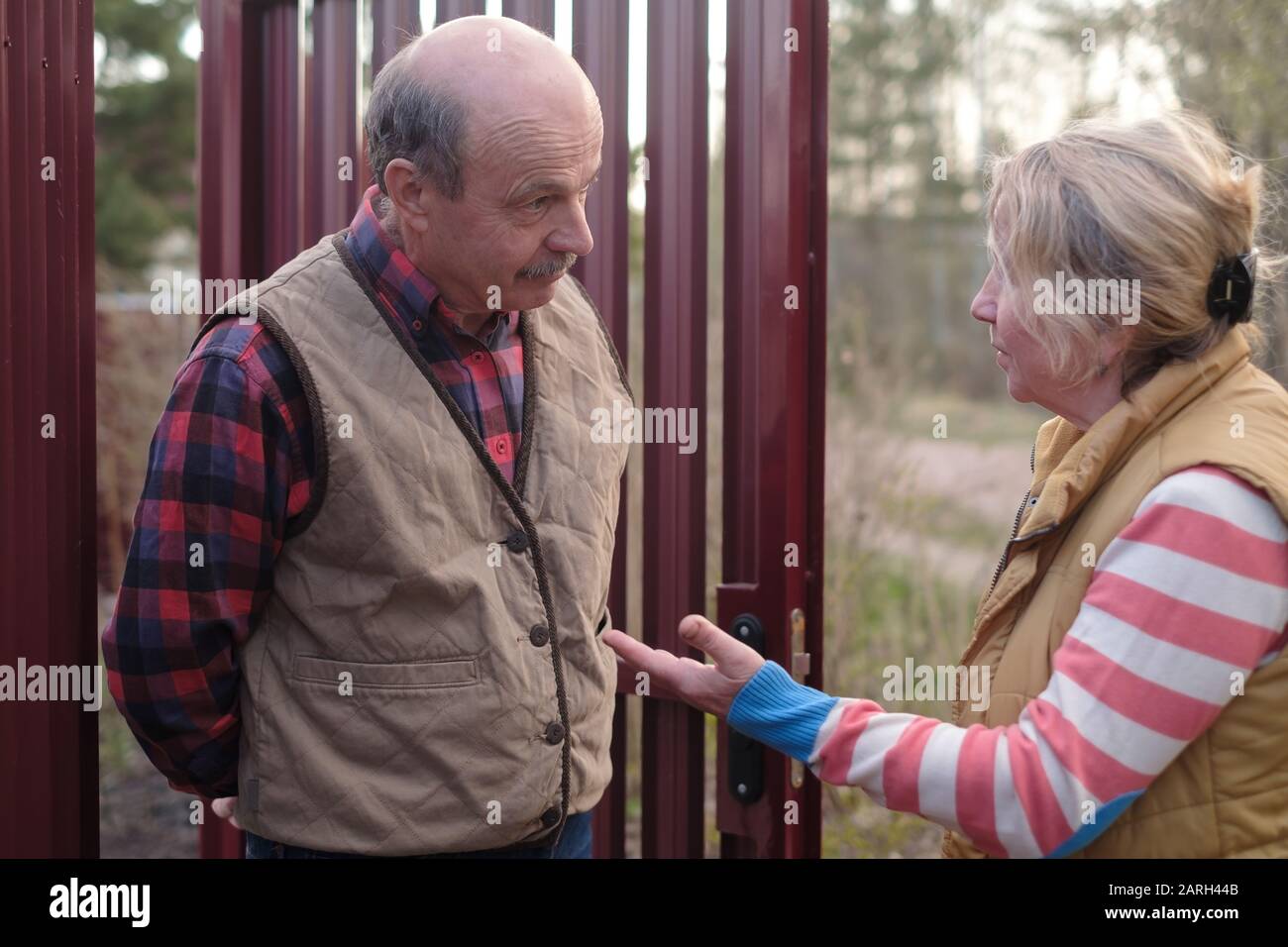 Rentnerin spricht mit einem älteren Mann in der Nähe von Zaun. Nachbarn diskutieren über Behauptungen, die unterschiedliche Meinungen haben. Stockfoto