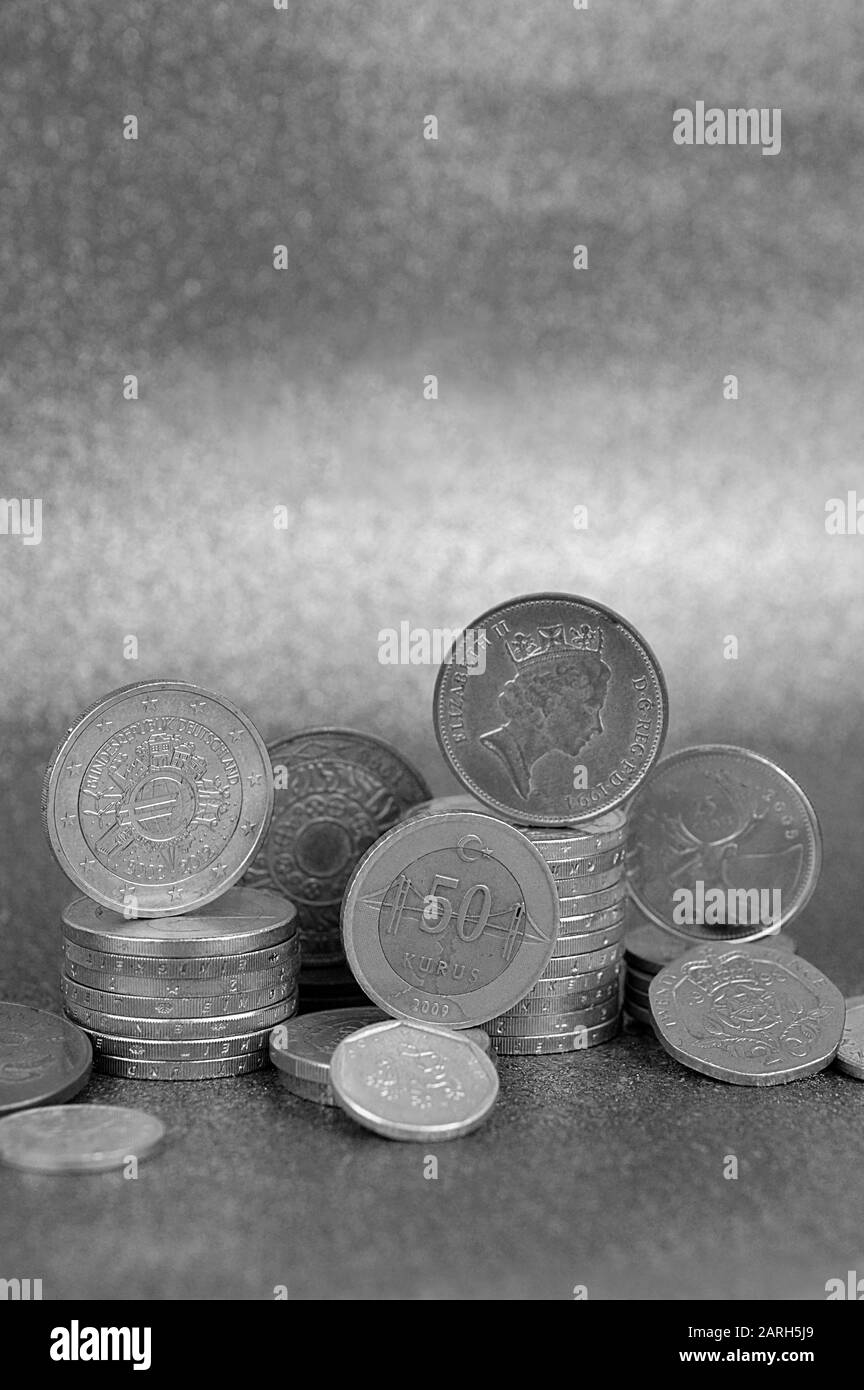 Münzstapel aus verschiedenen Nationen mit Euro und Cent vor silberfarbenem Hintergrund mit oben genauntem Kopierraum Stockfoto