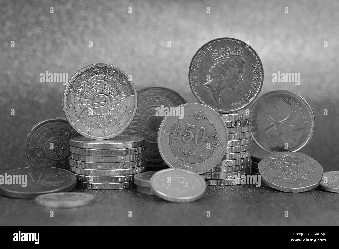 Münzstapel aus verschiedenen Nationen mit Euro und Cent vor silberfarbenem Hintergrund Stockfoto
