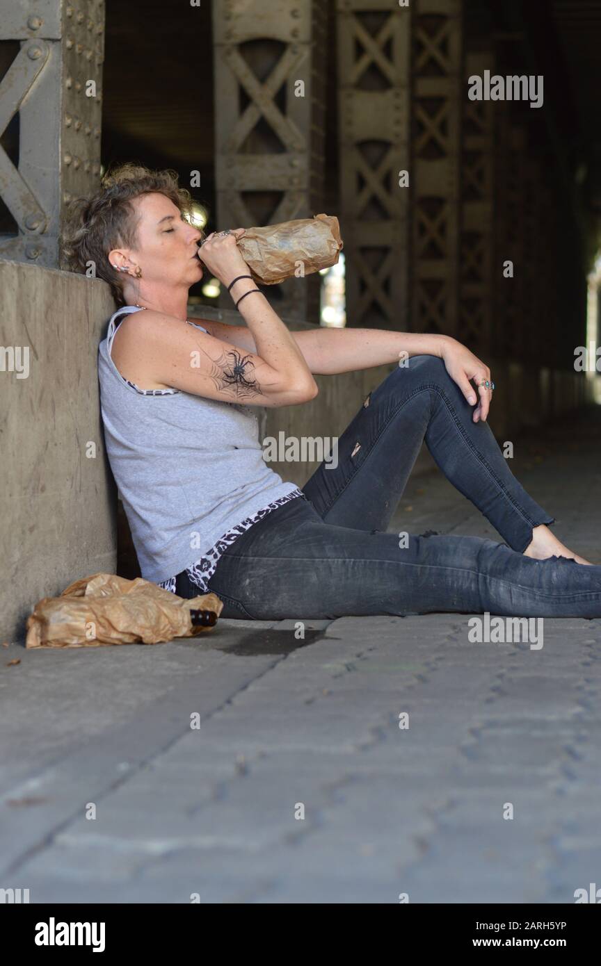 Eine Punkfrau unter einer Brücke trinkt Alkohol aus einer Flasche in einer braunen Papiertüte Stockfoto