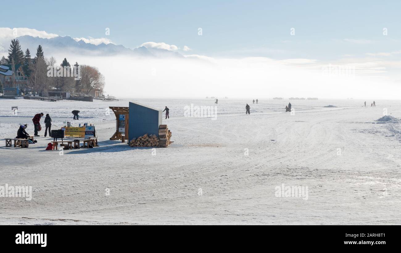 Invermere, British Columbia, Kanada - 25. Januar 2020: Zahlreiche Menschen Eisskaten und Eisfische auf dem gefrorenen Lake Windermere an einem nebligen Tag Stockfoto