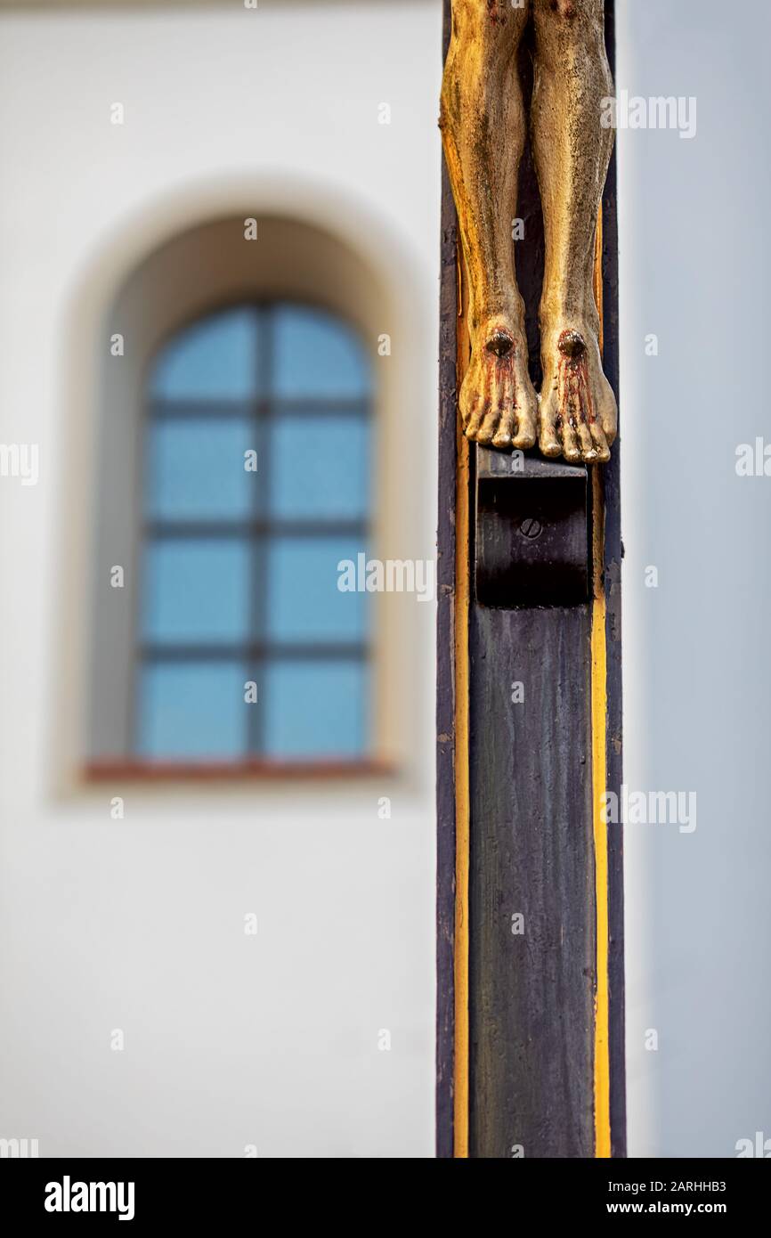 Teilansicht eines christlichen Holzkreuzes, nur die Füße Christi, im Hintergrund das Fenster einer Kirche Stockfoto