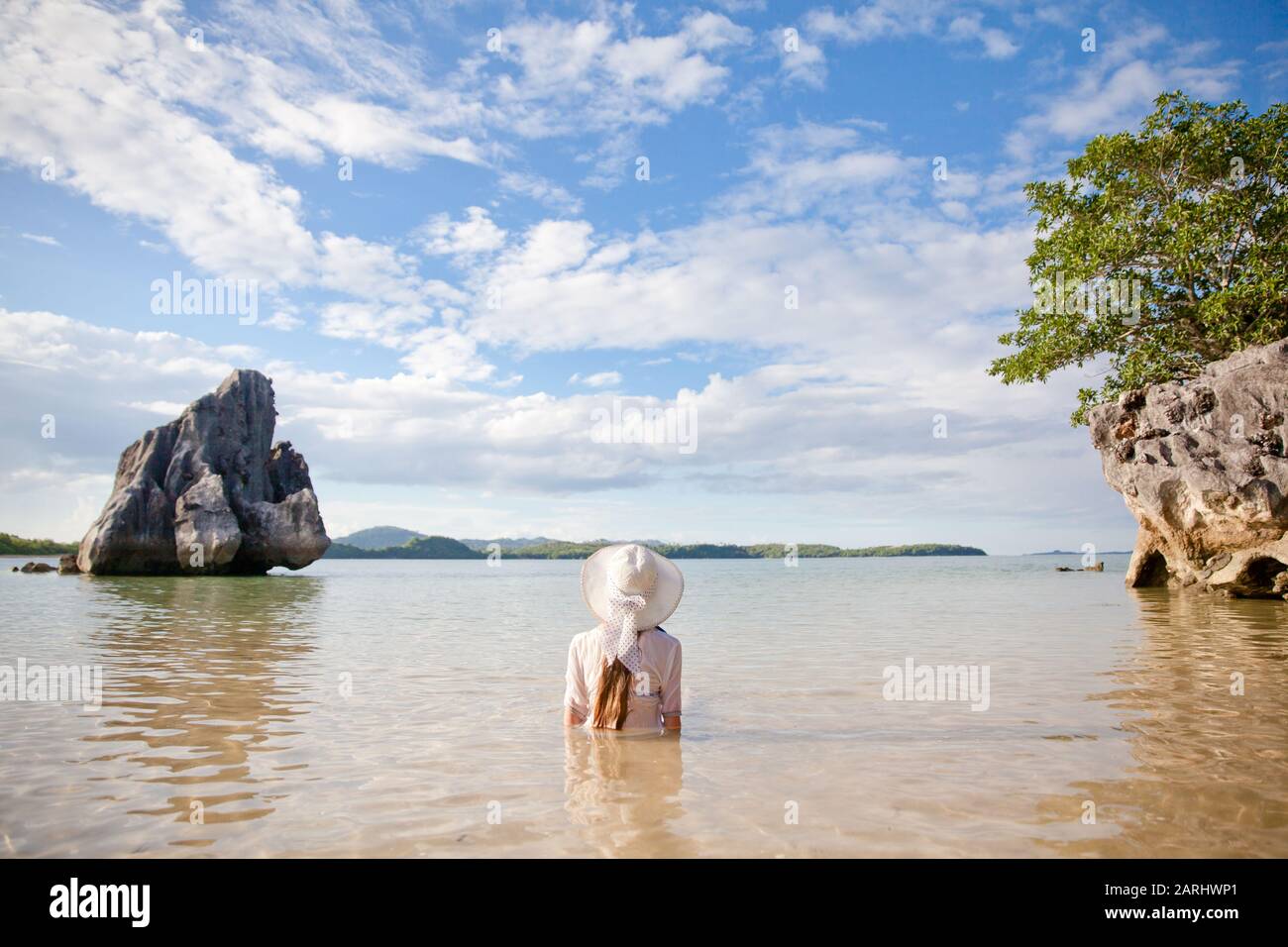Ein junges Mädchen in einem weißen Hut sitzt im Wasser auf einer tropischen Insel und genießt einen Urlaub. Sommer- und Urlaubskonzept Stockfoto