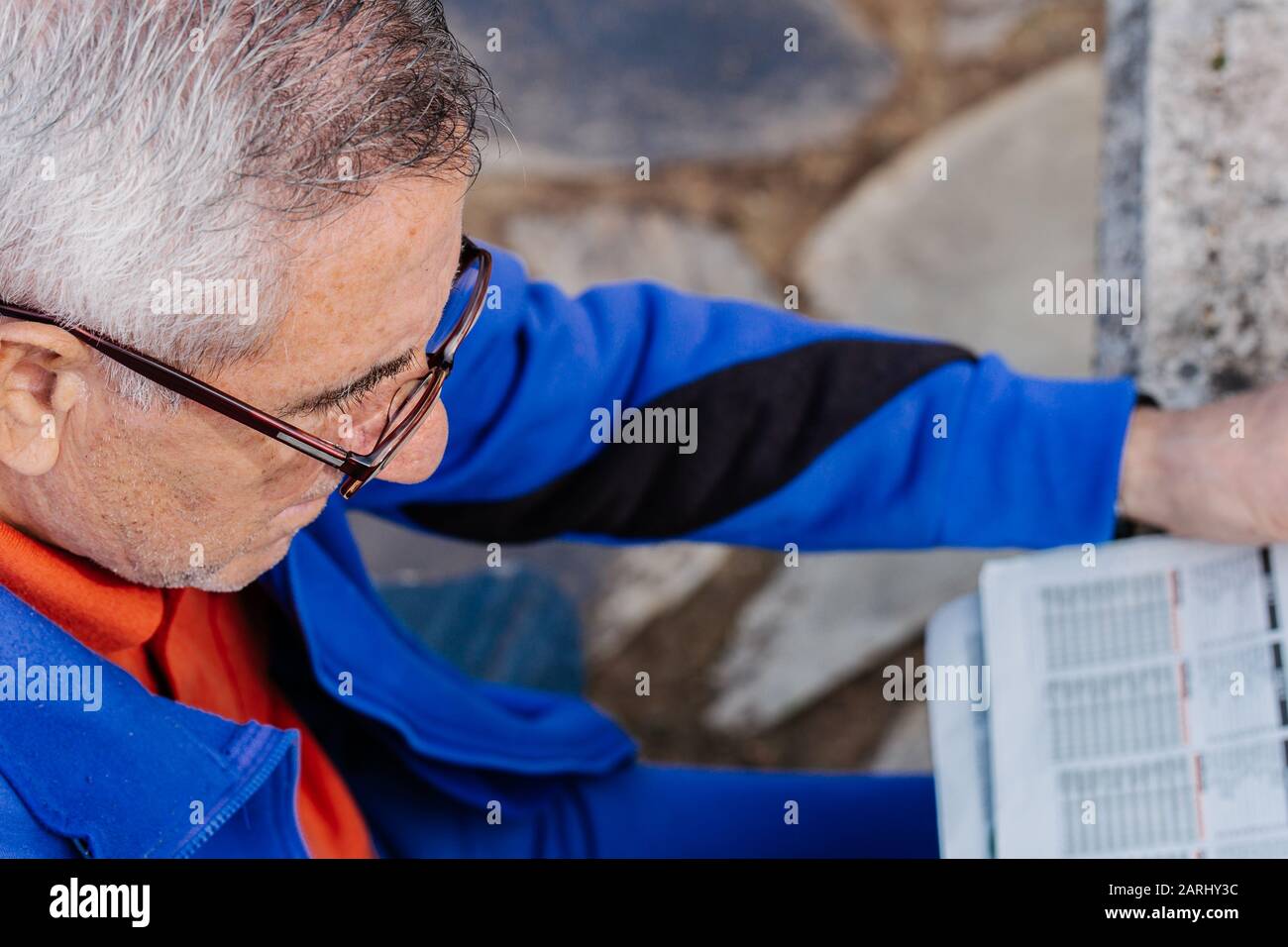 Alter Mann mit Brille liest die Zeitung im Park mit dem Boden im Hintergrund Stockfoto