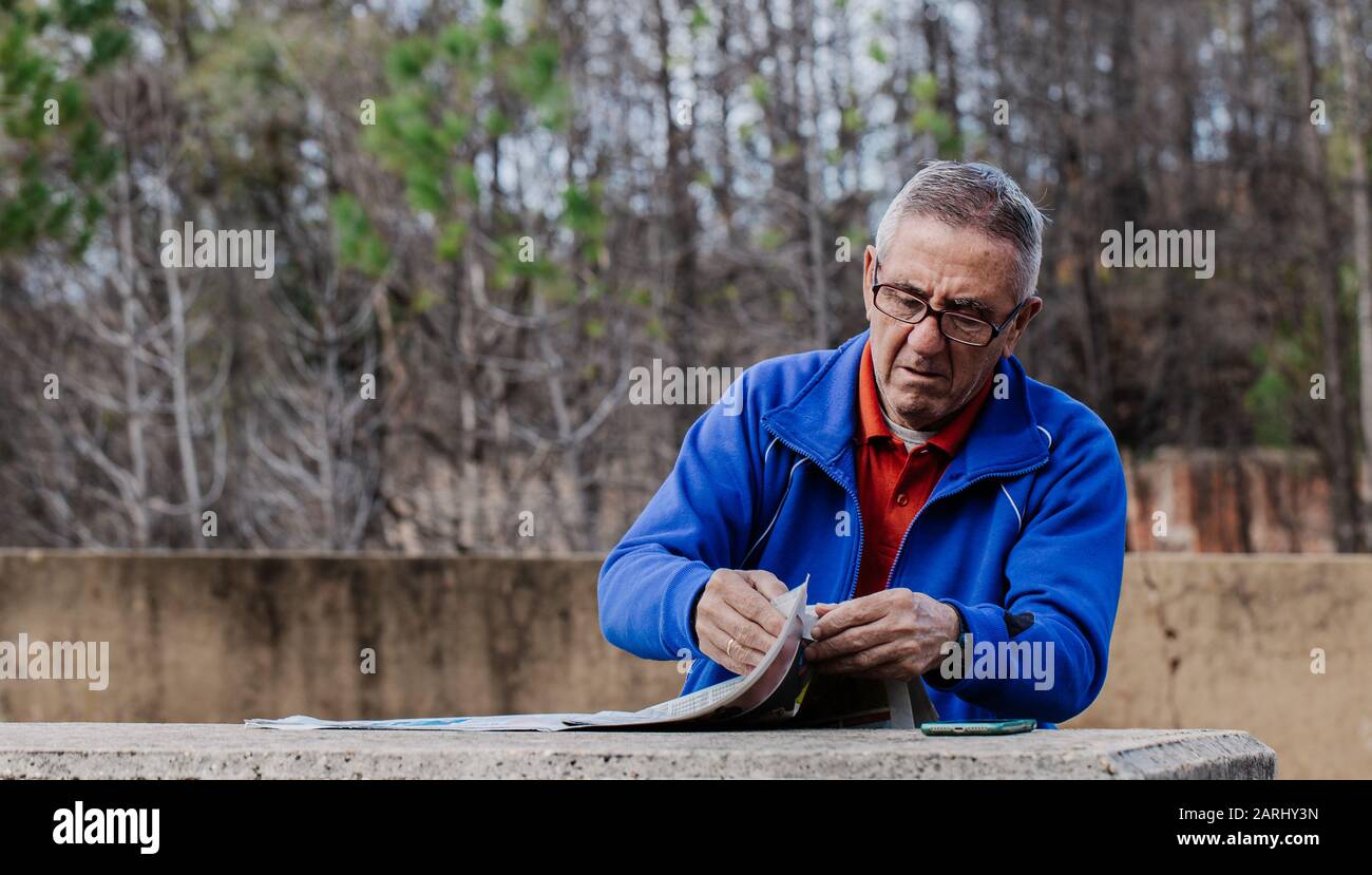 Alter Mann mit Brille liest die Zeitung im Park mit den Bäumen im Hintergrund Stockfoto