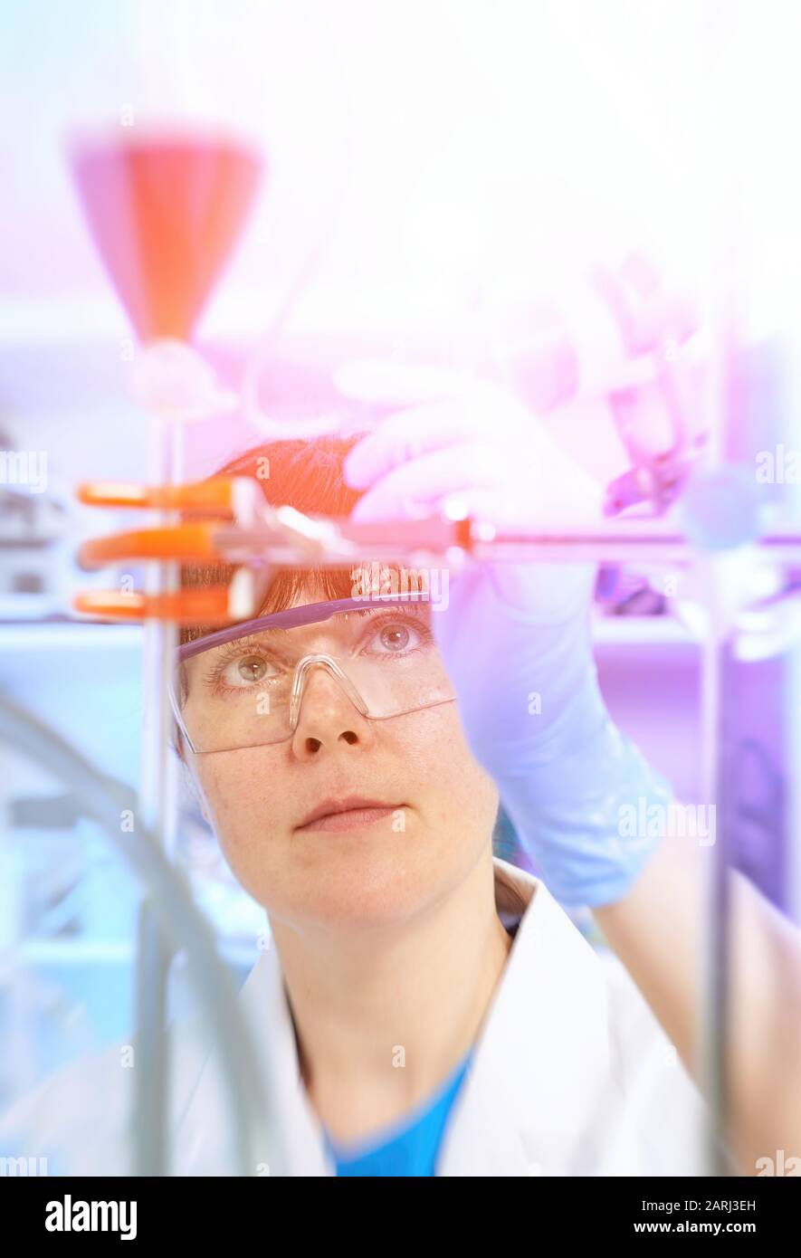 Junge Wissenschaftlerin oder Tech in Schutzkleidung überwacht die chemische Synthese und überprüft die Reaktion. Labor, Glaswaren, futuristisch violett Neon LIGH Stockfoto