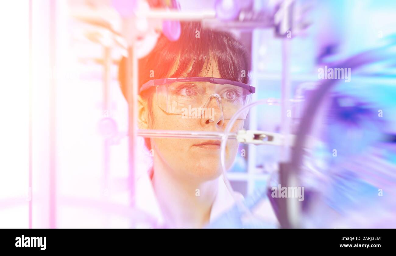 Junge Wissenschaftlerin oder Tech in Schutzkleidung überwacht die chemische Synthese und überprüft die Reaktion. Labor, Glaswaren, futuristische Orange und Püpl Stockfoto