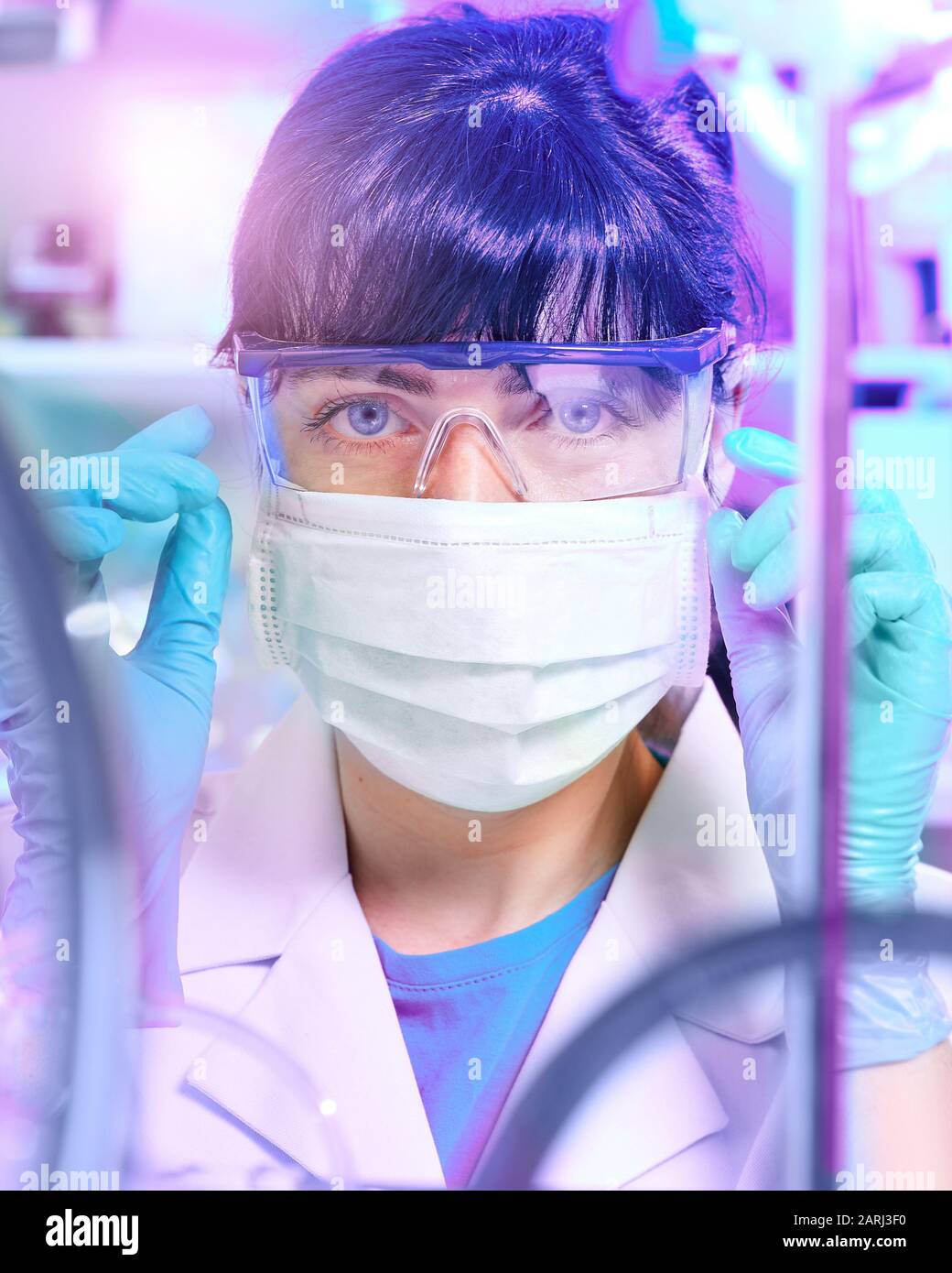 Junge Wissenschaftlerin oder Tech in Schutzkleidung überwacht die chemische Synthese und überprüft die Reaktion. Labor, Glaswaren, futuristisches Türkis und PU Stockfoto