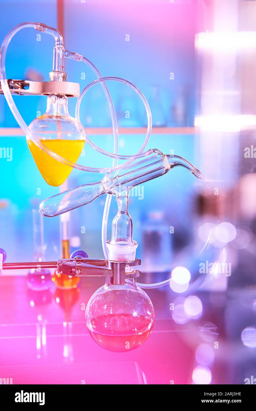 Laufende Reaktion im Labor für organische Chemie, Destillationsglas, Laborglasgeräte. Futuristische Neonleuchten, auffälliger violetter, pinker, Stockfoto