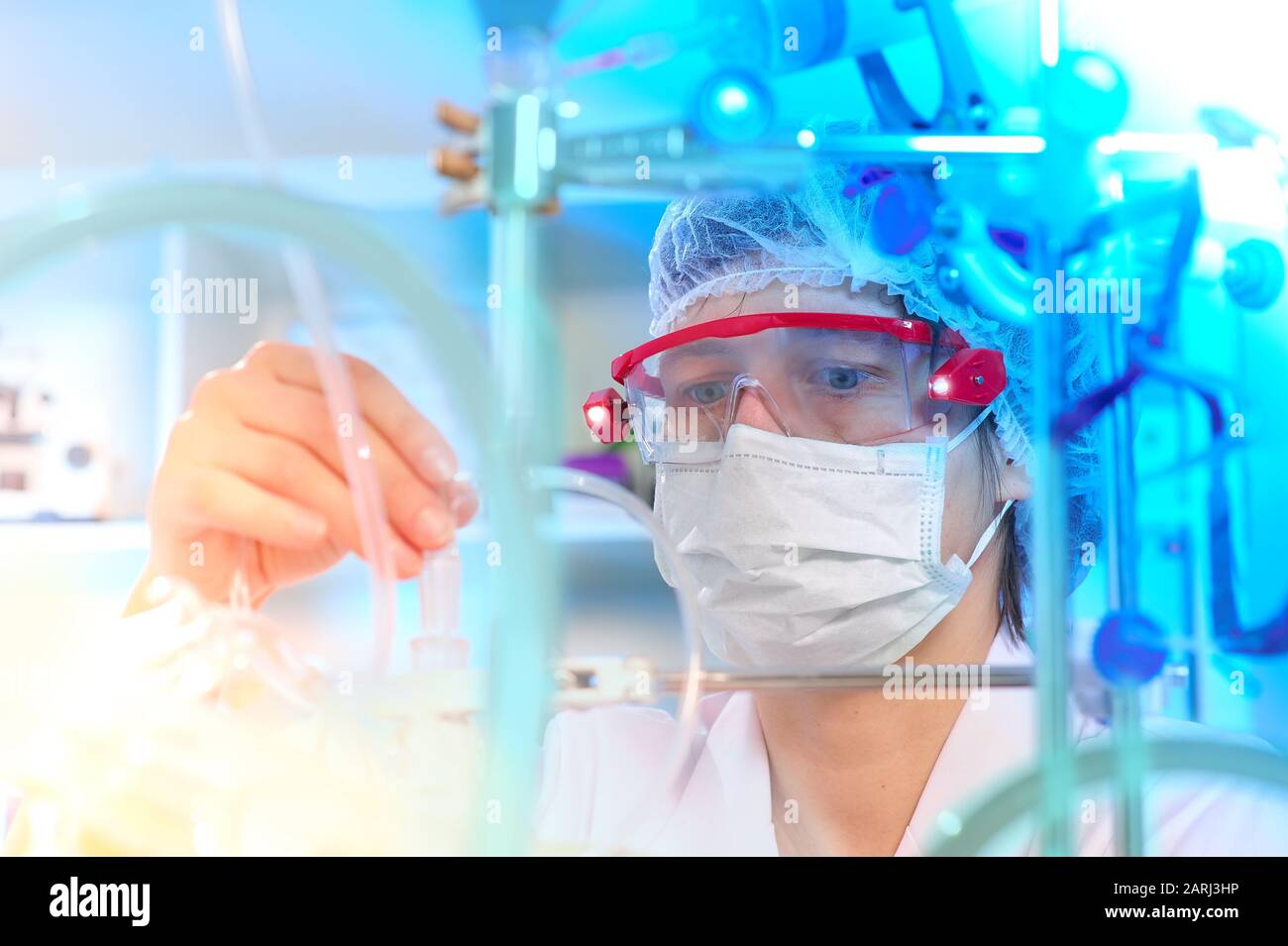 Junge Wissenschaftlerin oder Tech in Schutzkleidung überwacht die chemische Synthese und überprüft die Reaktion. Labor, Glaswaren, futuristisches blauweißes Licht Stockfoto