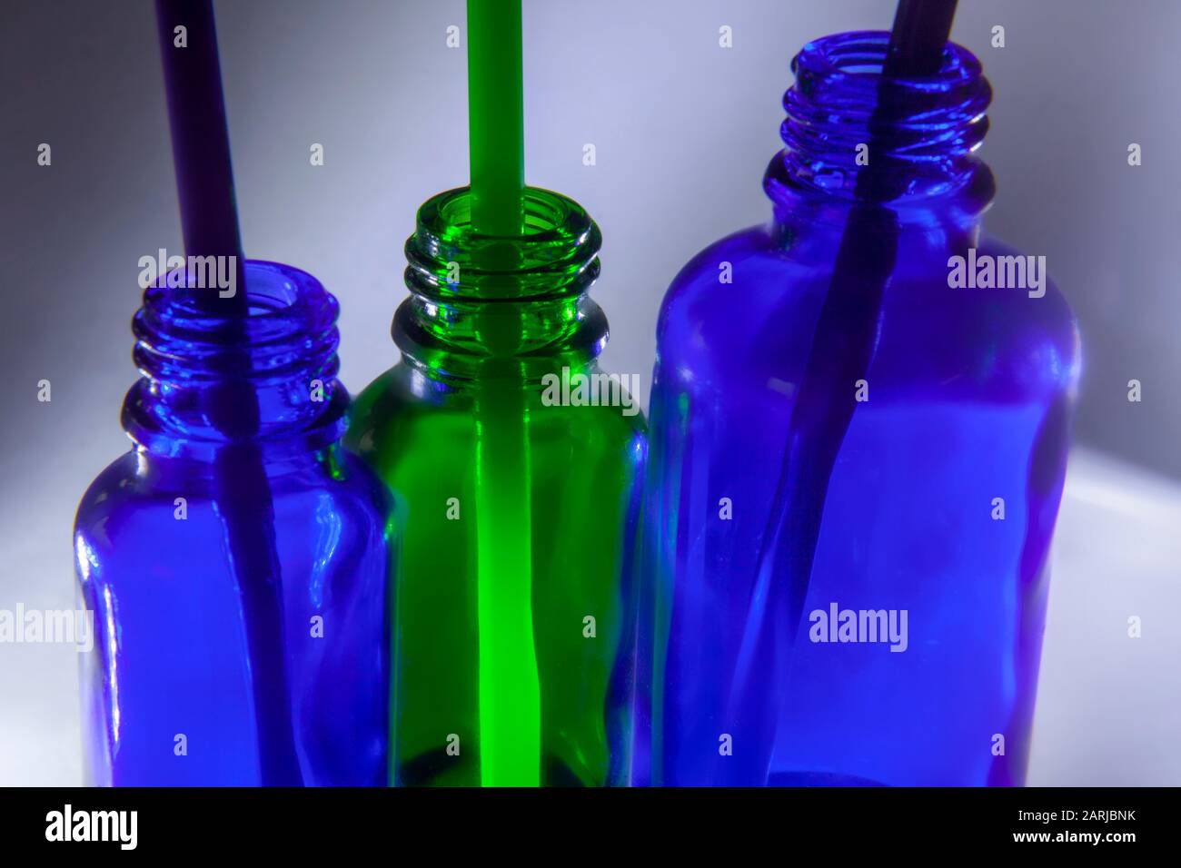 Drei kleine grüne und zwei blaue Flaschen mit Strohhalmen auf weißem und grauem Hintergrund Stockfoto