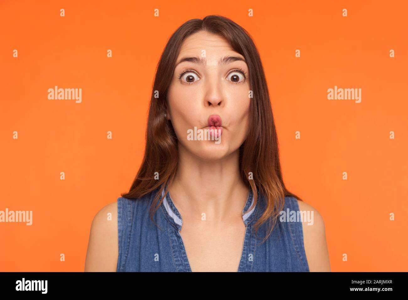 Nahaufnahme der lustigen dummen brünetten Frau, die Fisch ins Gesicht stellt, mit großen, verwunschenen Augen und idiotischer albern Ausdrucksweise, die lächerlichen Grimace zeigen Stockfoto