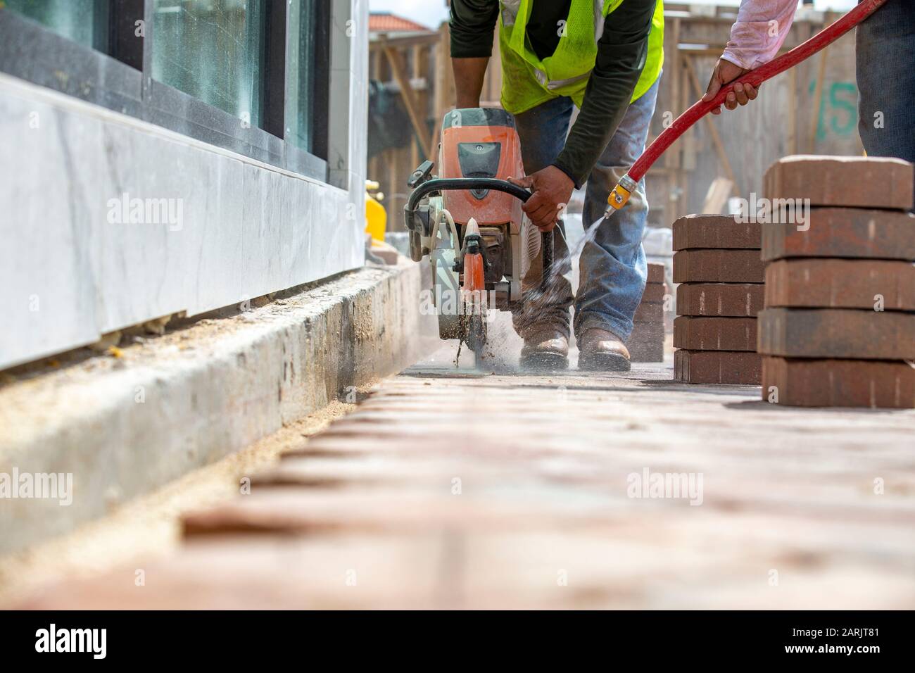 Baufertiger arbeiten an einem Arbeitsplatz, einer schneidet die Backsteine in gerader Linie und der andere kühlt die Klinge mit Wasserspray. Stockfoto