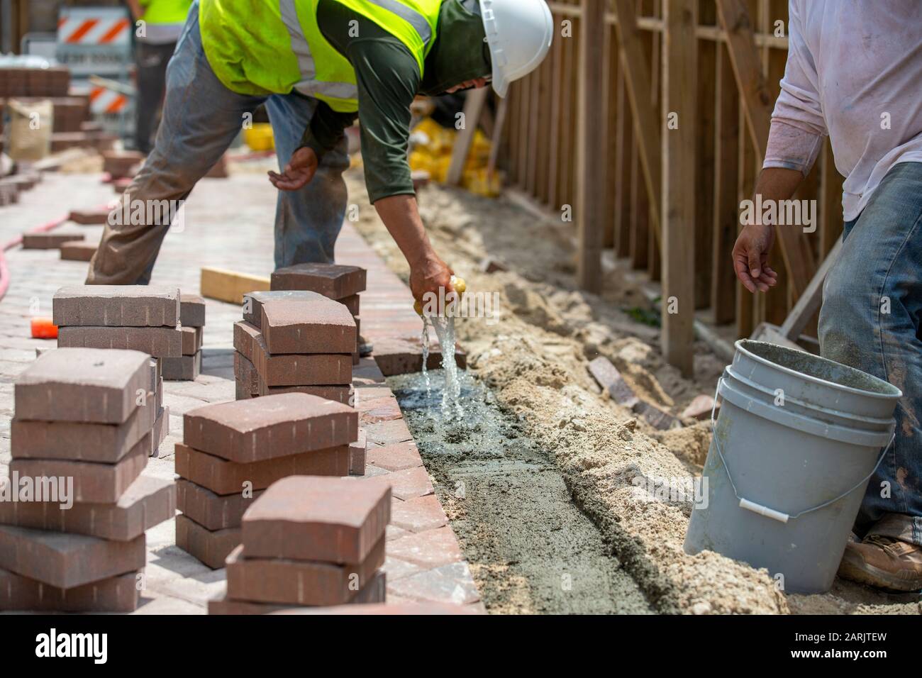Backstein-Schicht oder Bauarbeiter gießen etwas Beton, um einige Pflastersteine auf zu legen, um optimale Ergebnisse zu erzielen. Stockfoto