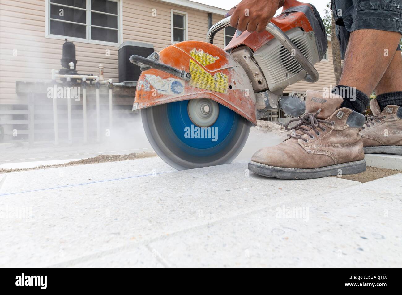Bauarbeiter, Ziegelschicht, Straßenfertiger, der eine Kachel auf dem Pooldeck eines Wohnsitzes mit einer schweren Steinsäge zerschneidet, die Staub erzeugt. Stockfoto