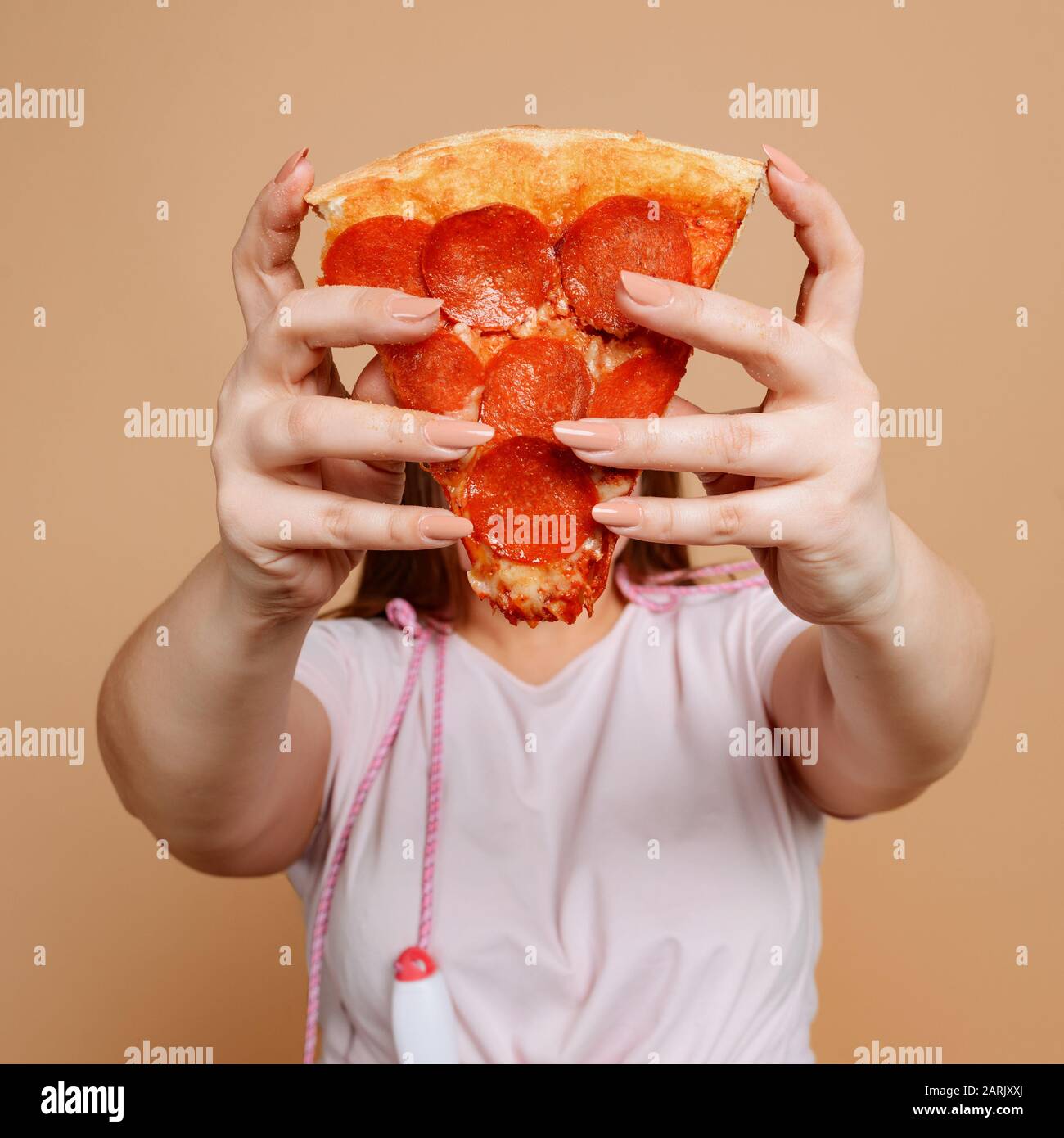 Mädchen bedeckt Gesicht mit Pizza Scheibe. Überessen und Fettleibigkeit Stockfoto